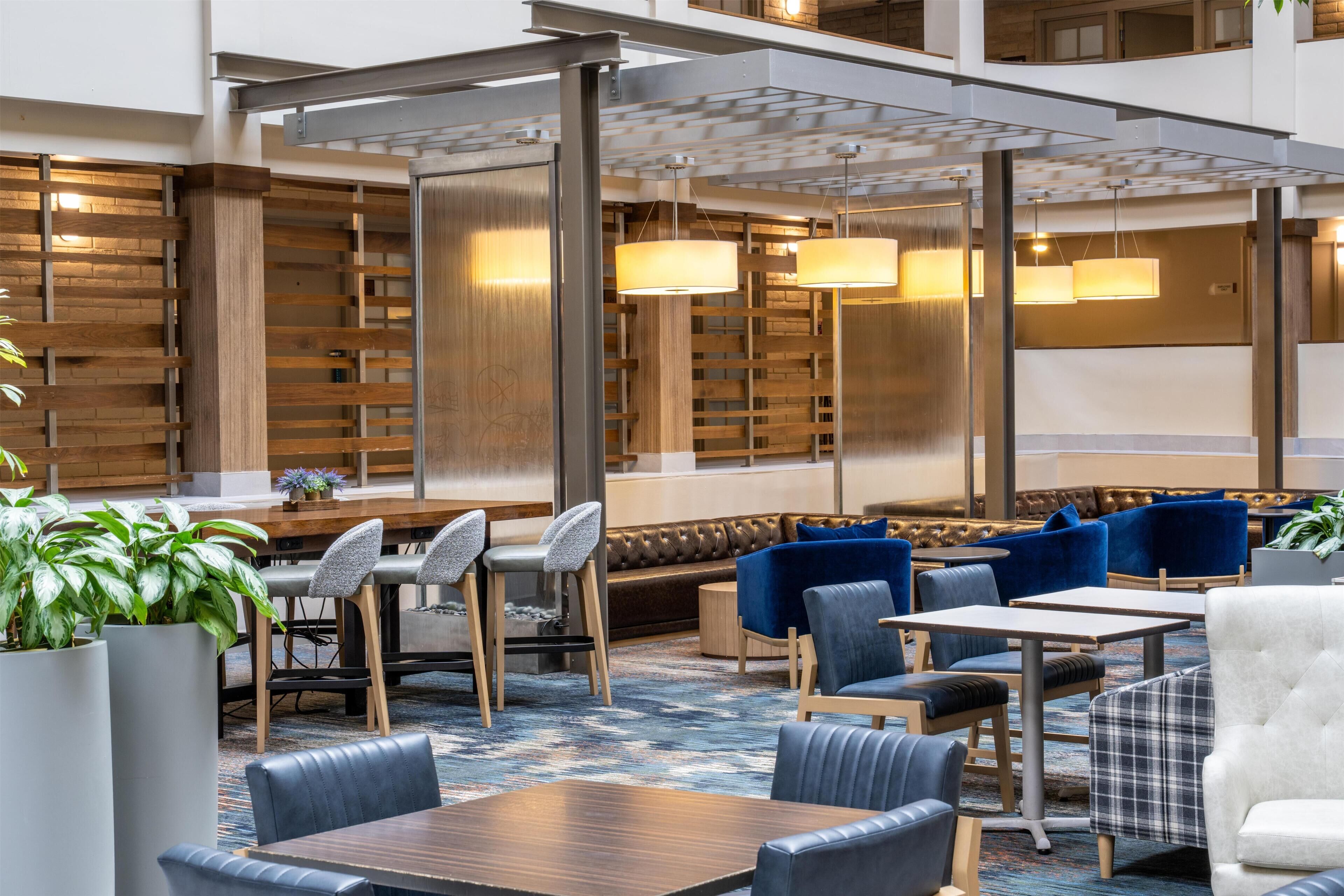 A modern hotel lobby with seating areas, tables, and hanging lamps.