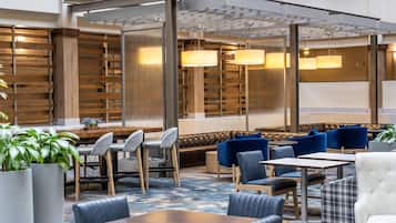A modern hotel lobby with seating areas, tables, and hanging lamps.