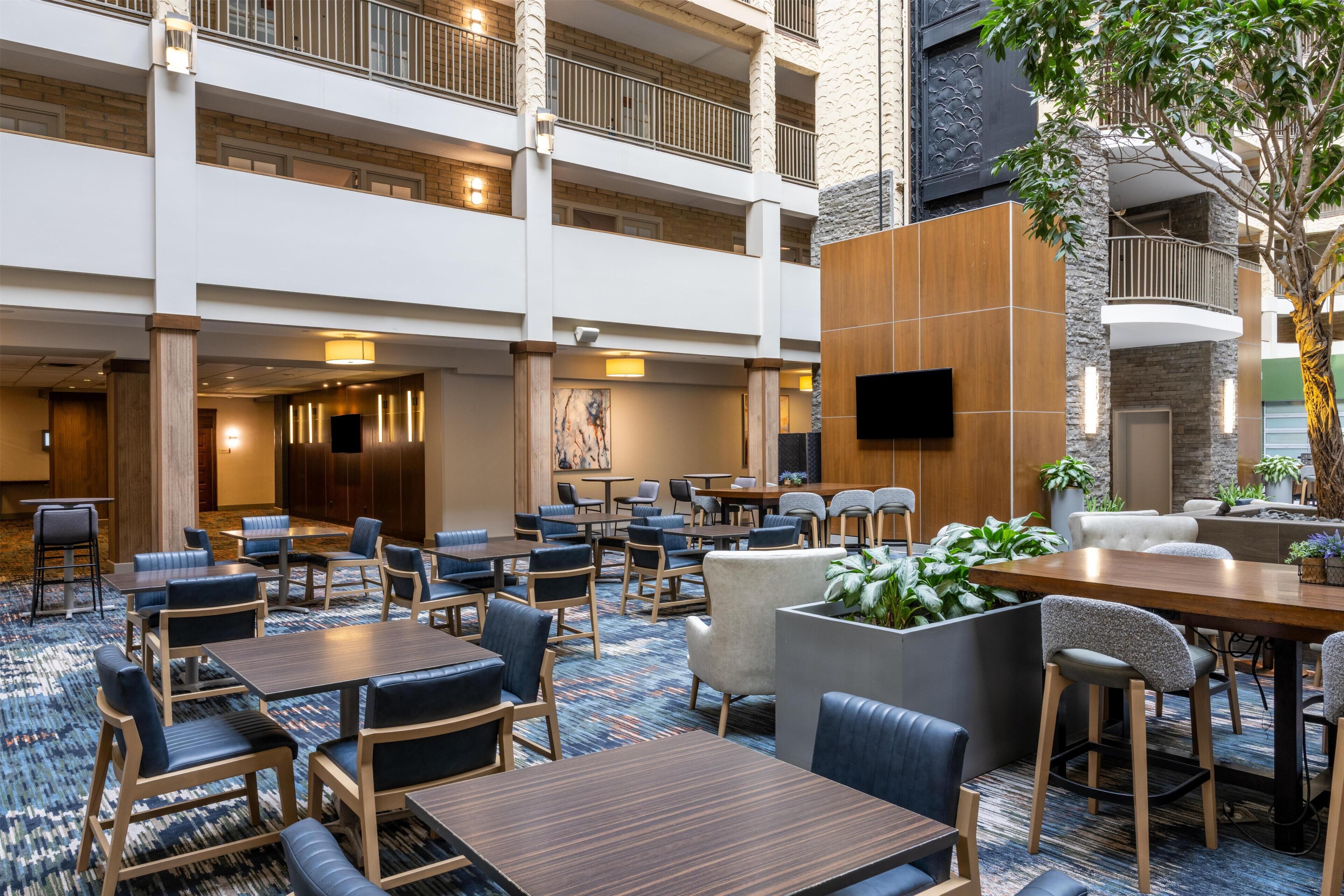 A multi-level hotel lobby with seating areas, a flat-screen TV, and a large plant.