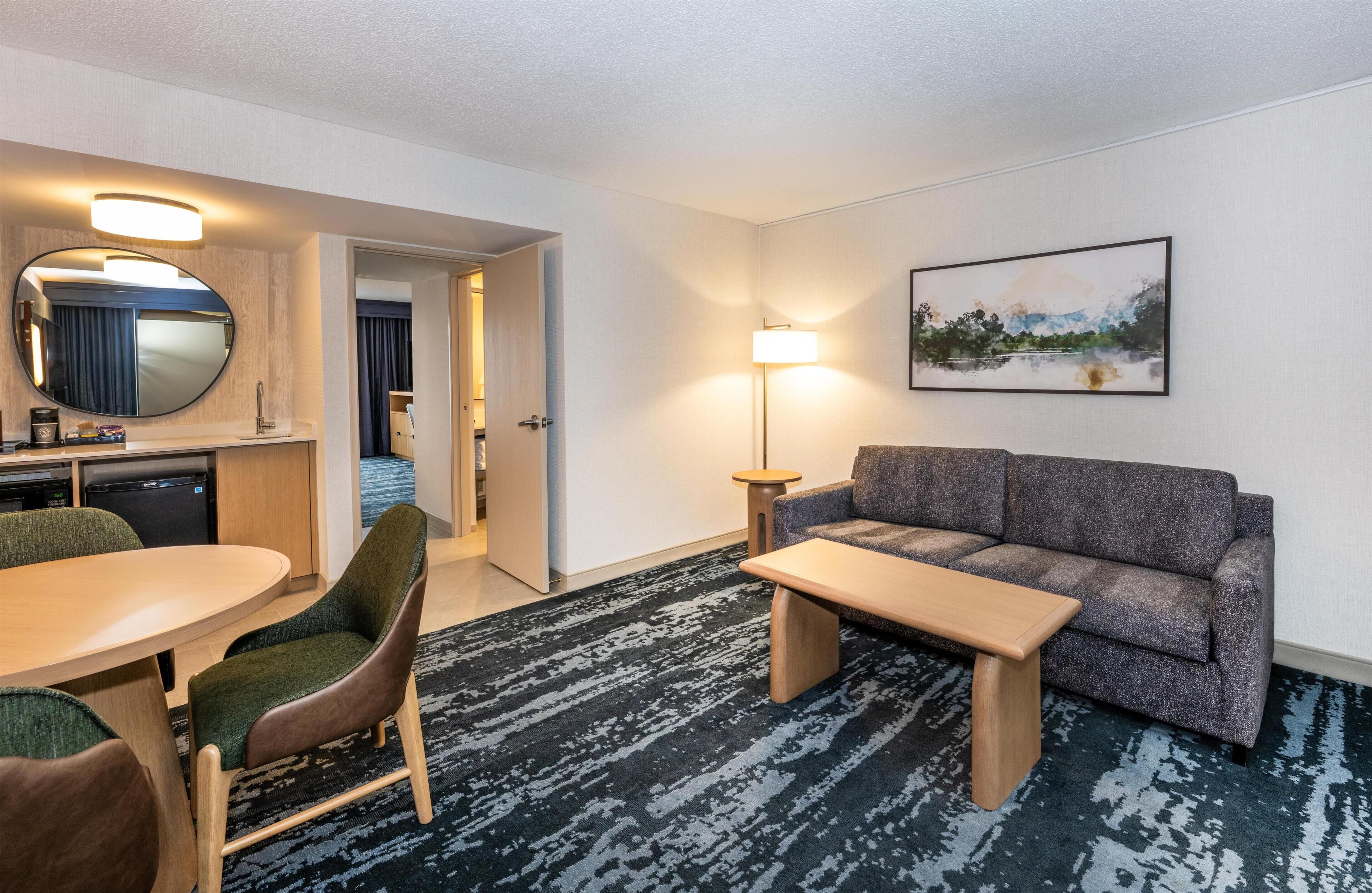 Et hotelværelse med spiseplads, sofa, lampe, et billede og udsigt til det fri.