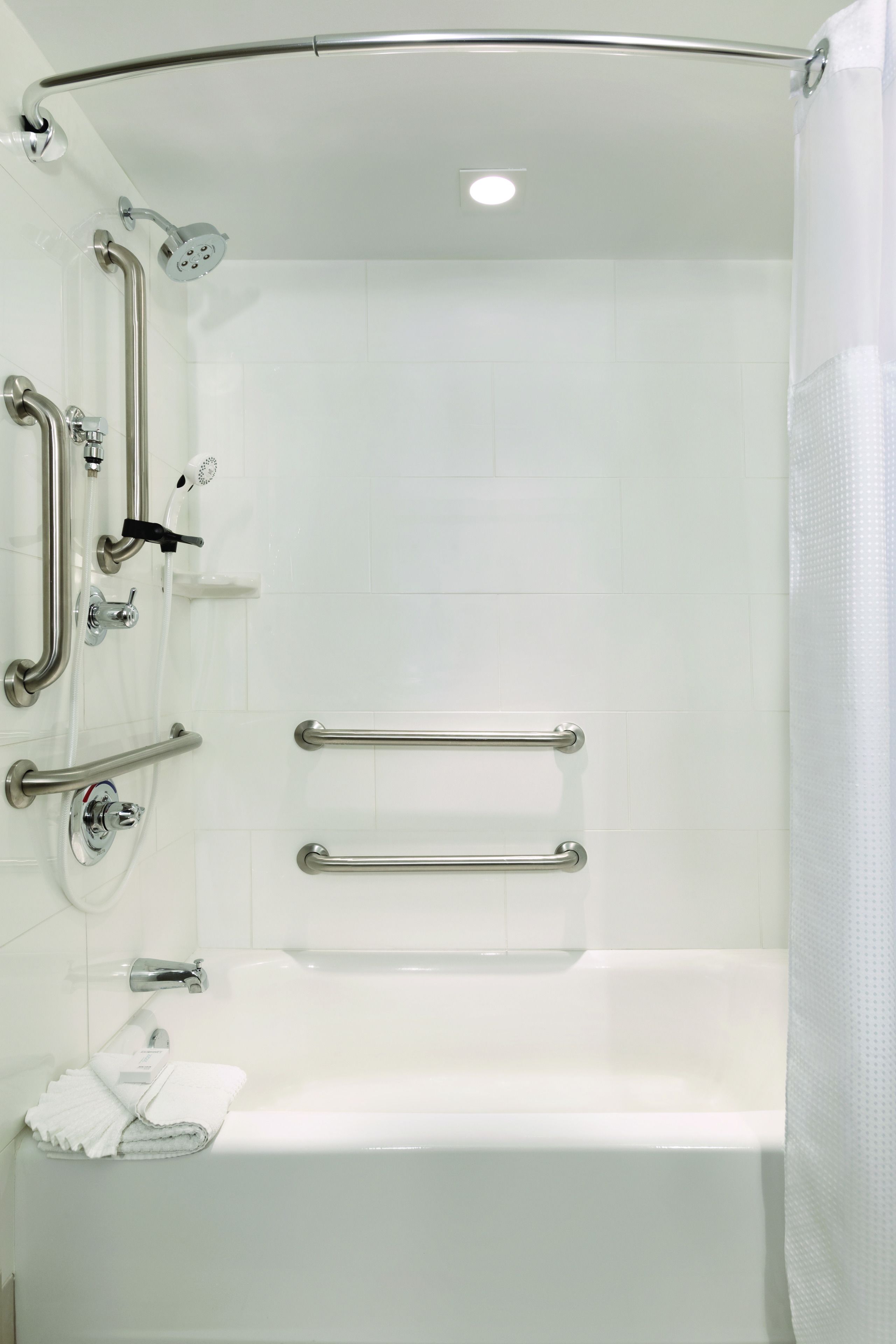Un baño moderno con cabina de ducha, barras de apoyo y pared cubierta de azulejos blancos.