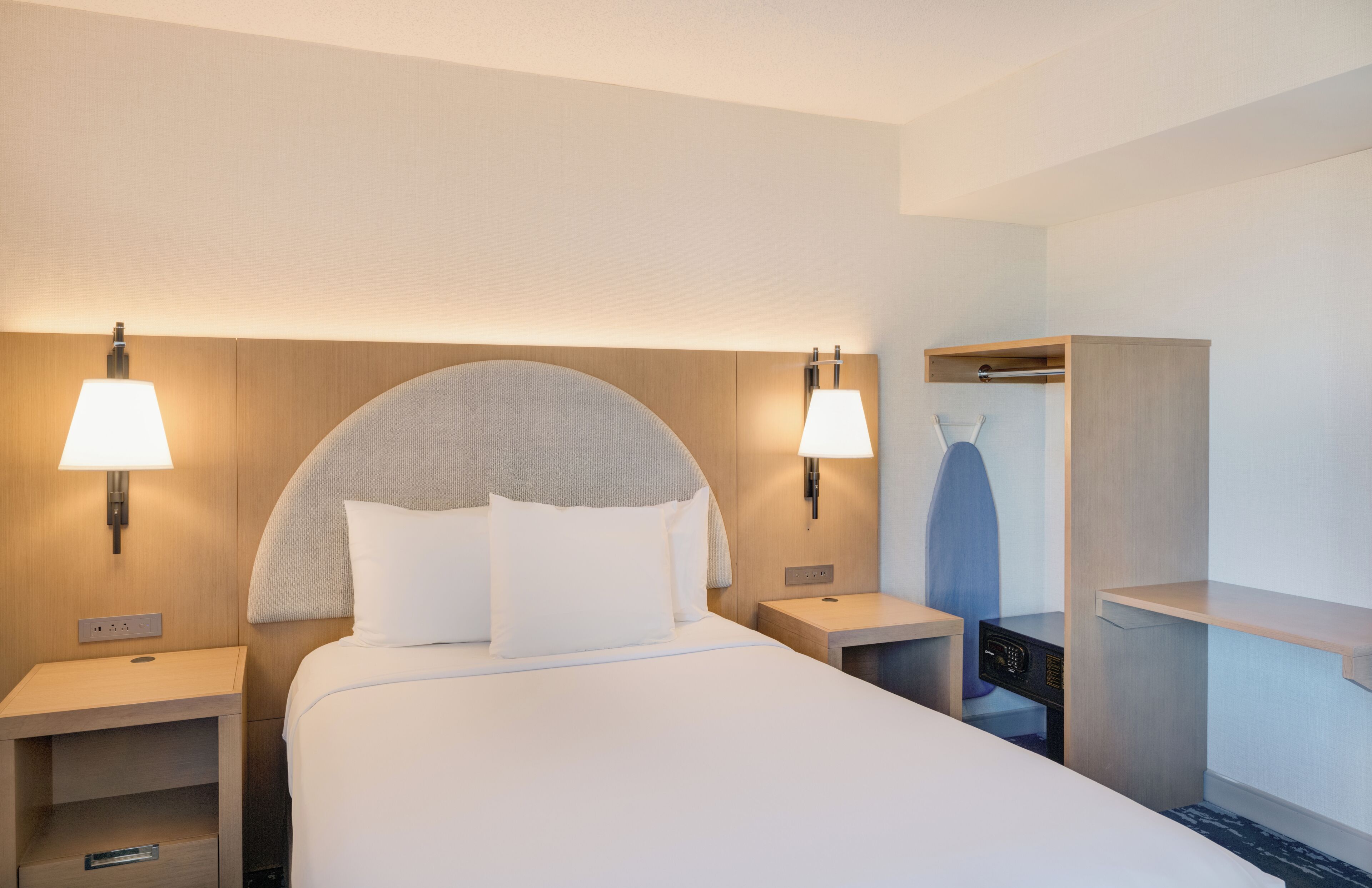 Habitación de hotel con una cama grande, dos mesitas de noche, un armario y lámparas fijadas a la pared.