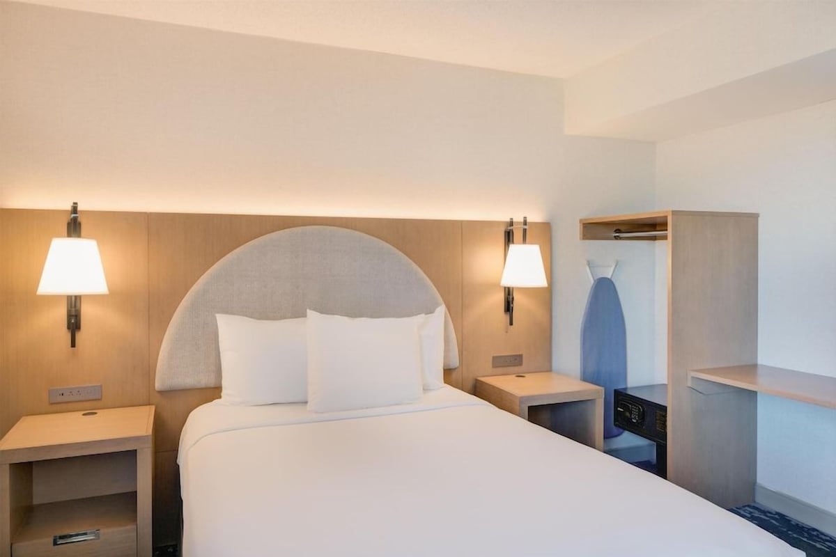 A hotel room with a large bed, two bedside lamps, a wardrobe, and a small table.