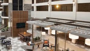 A modern hotel lobby with a checkered floor, a wooden reception desk, a seating area with sofas and chairs, and a TV mounted on the wall.