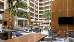A multi-level hotel lobby with a central atrium, seating areas, and a flat-screen TV mounted on the wall.