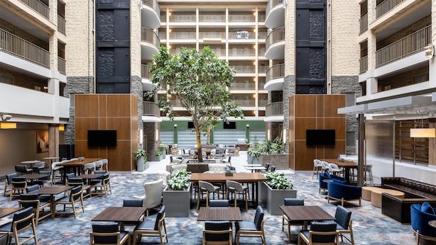 A hotel lobby with multiple seating areas, a central tree, and a view of the building's interior.