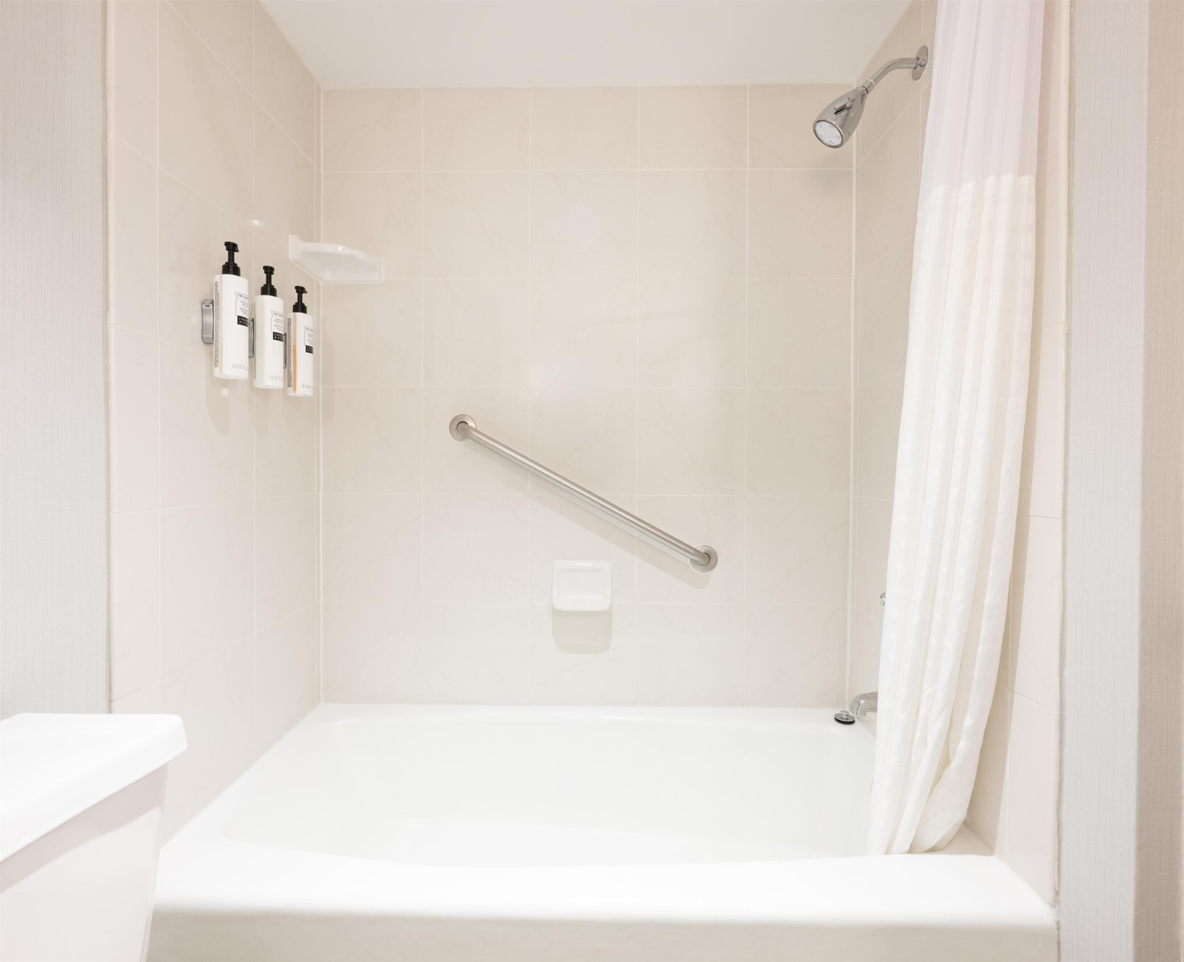 A bathroom with a bathtub, a shower, and a handrail.