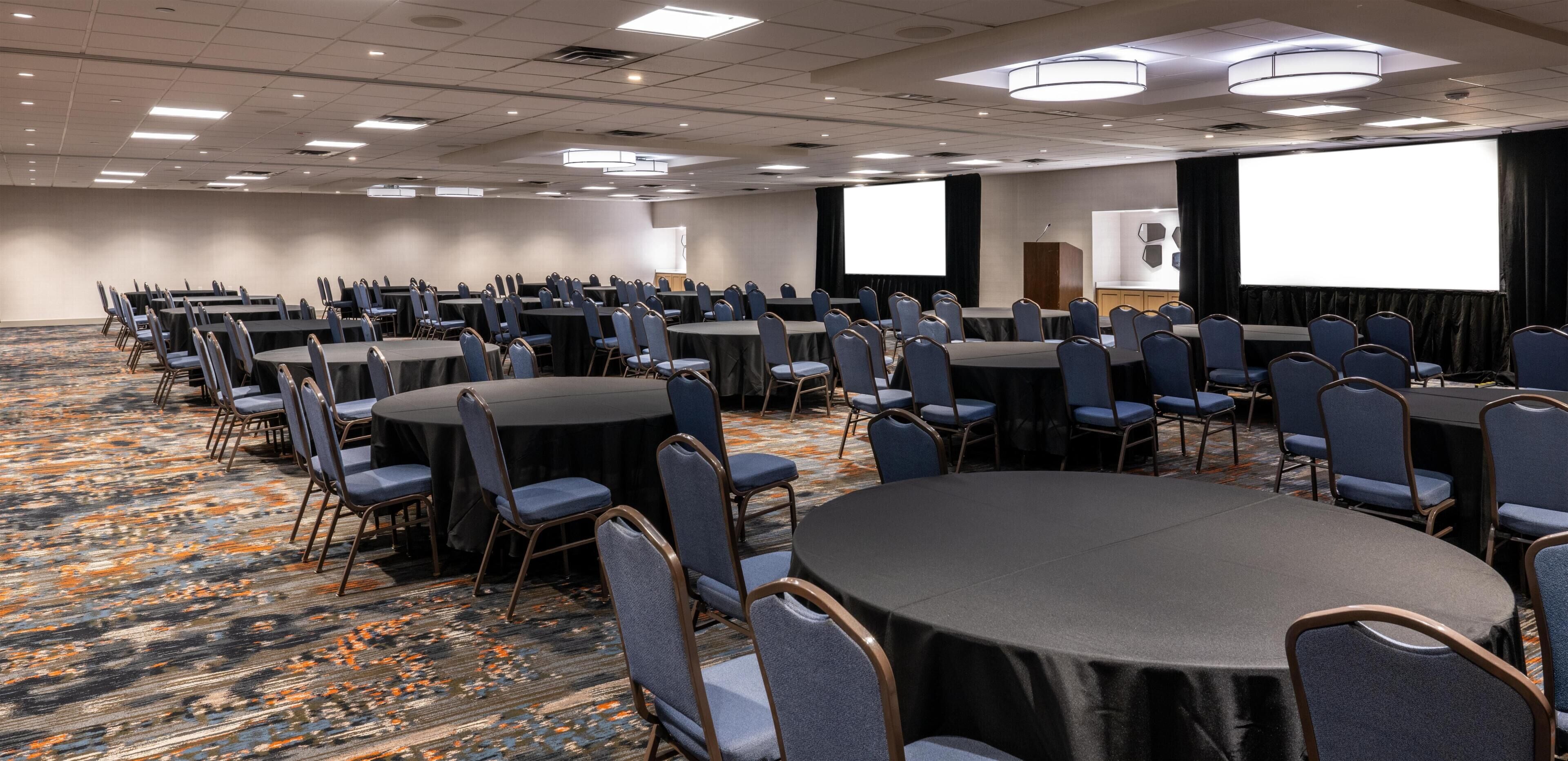 A conference room with multiple tables and chairs, a carpeted floor, and a projector screen.