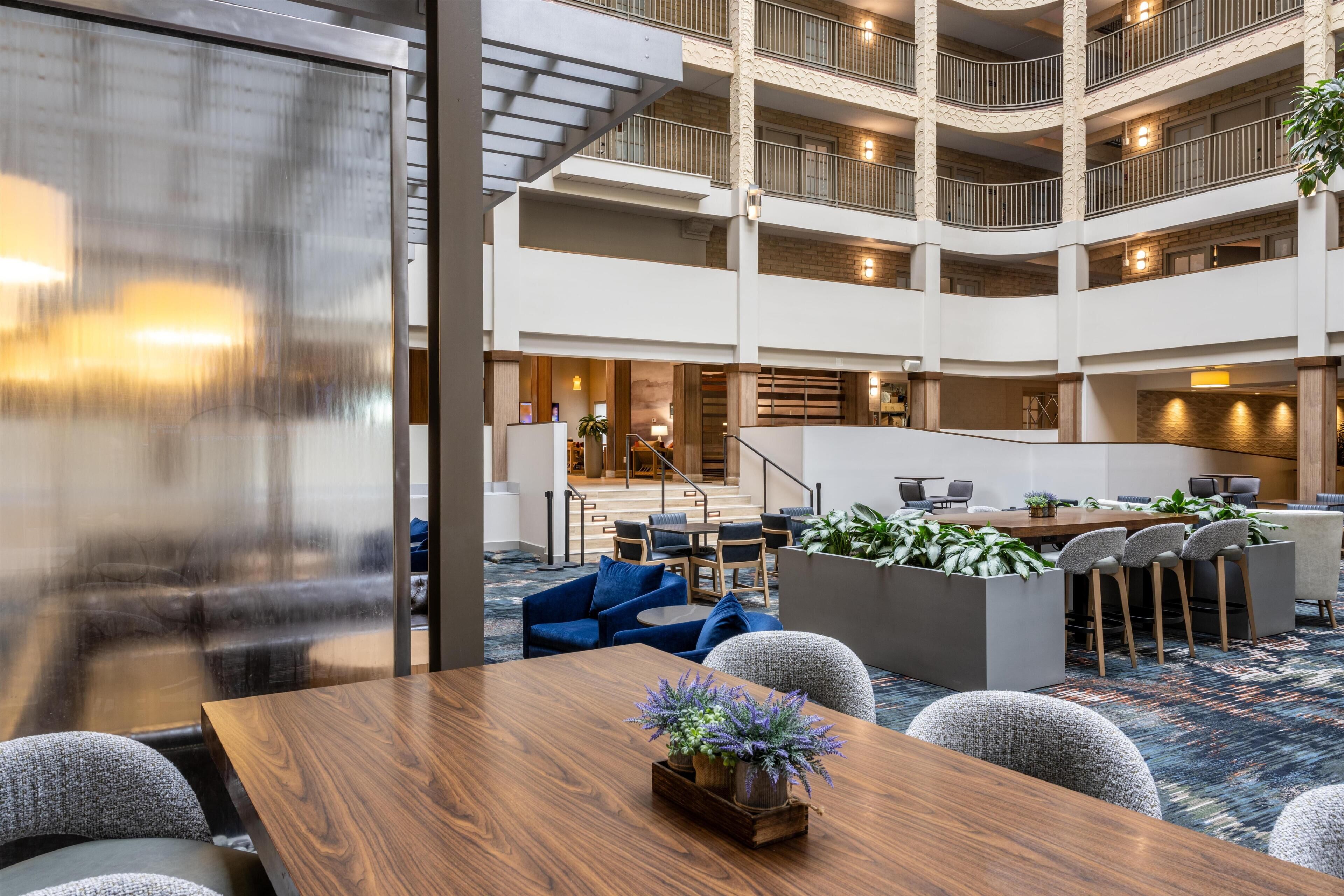 Un vestíbulo de hotel de varios niveles con una escalera central, zonas de estar y un mostrador de recepción.