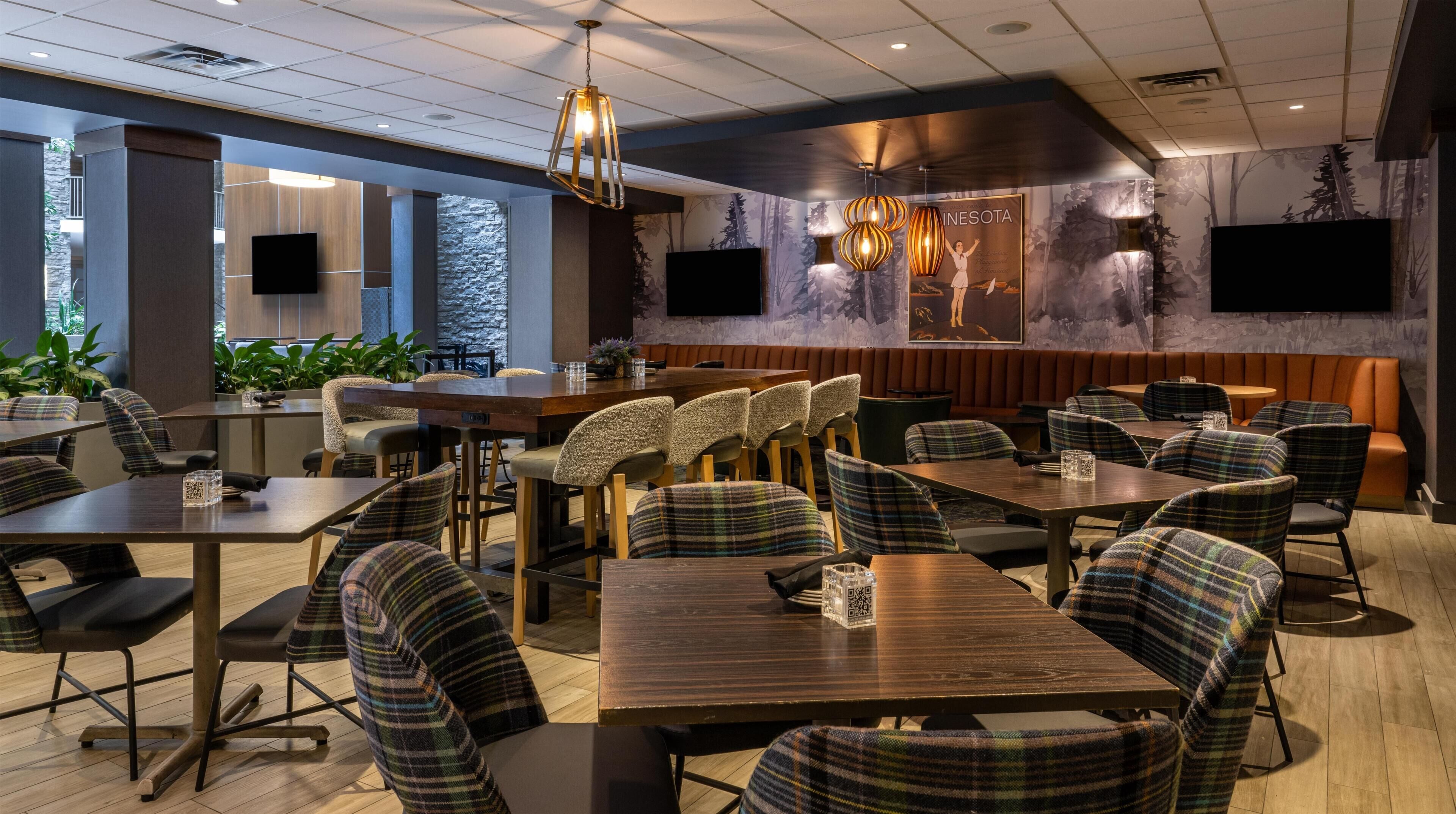 A modern restaurant with wooden tables and plaid chairs, a stone accent wall, and a large mural.