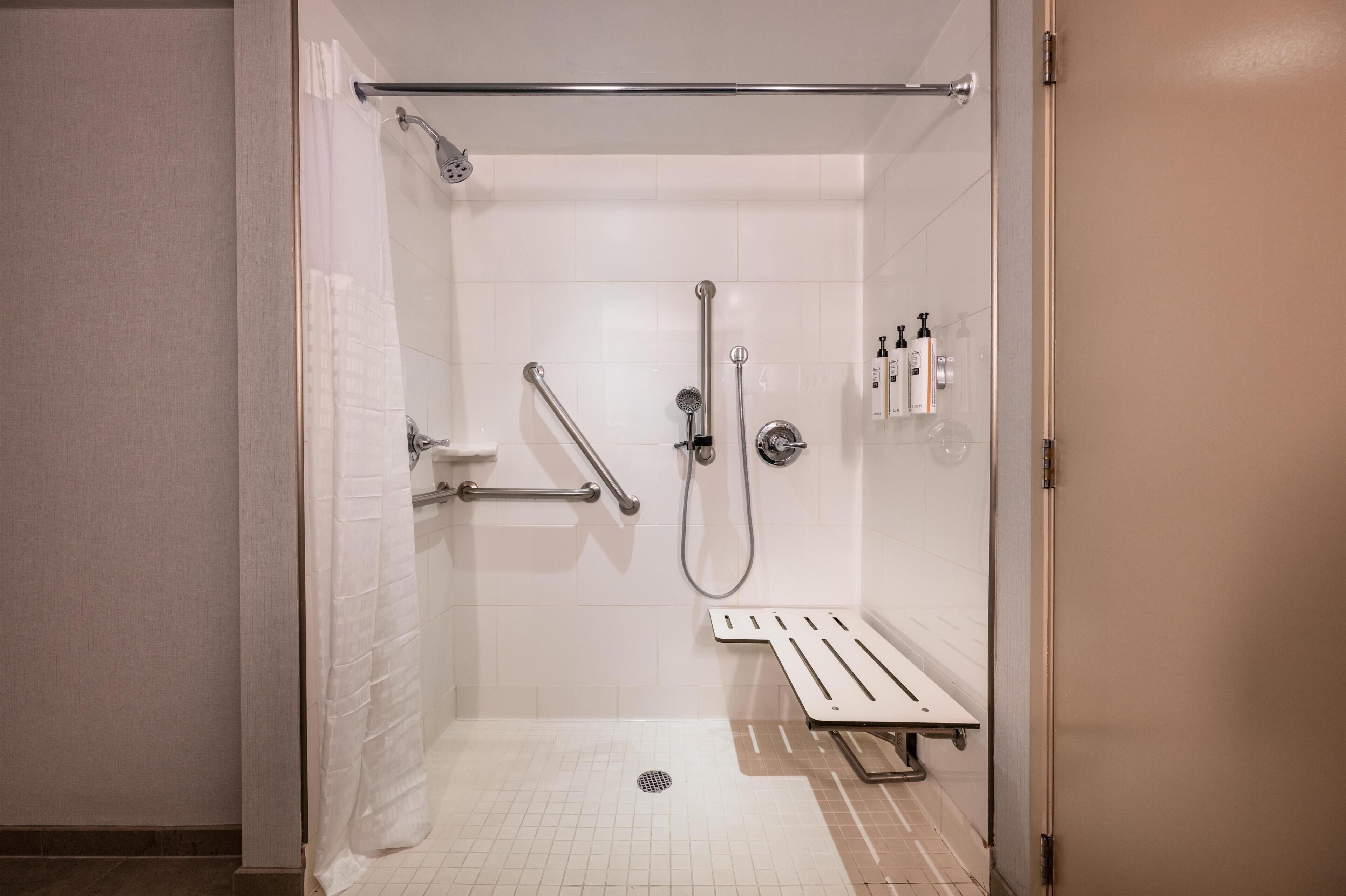 A walk-in shower with a grab bar, a handheld showerhead, and a seat.