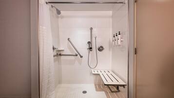 A walk-in shower with a grab bar, a handheld showerhead, and a seat.