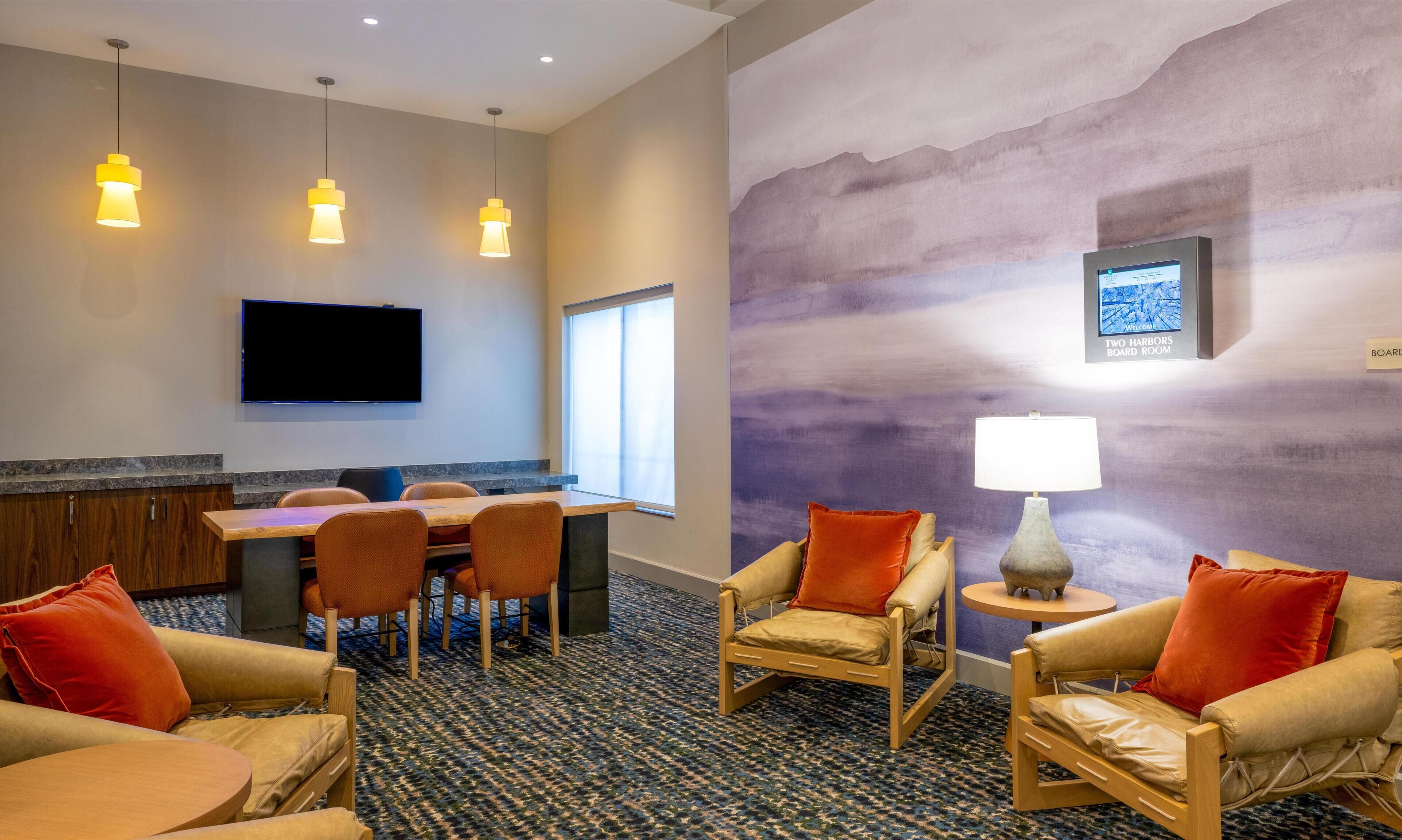 A conference room with a table, chairs, a TV, and a wall-mounted lamp.