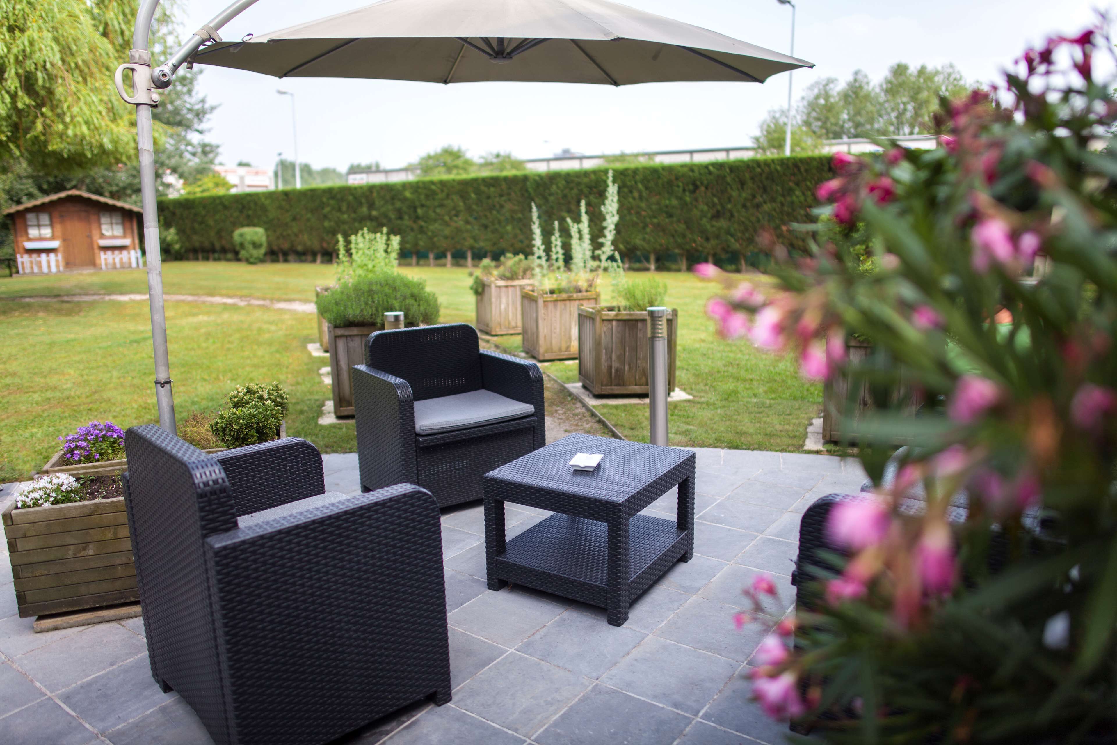 An outdoor patio area with wicker furniture, including a sofa and two side tables, under a large umbrella.