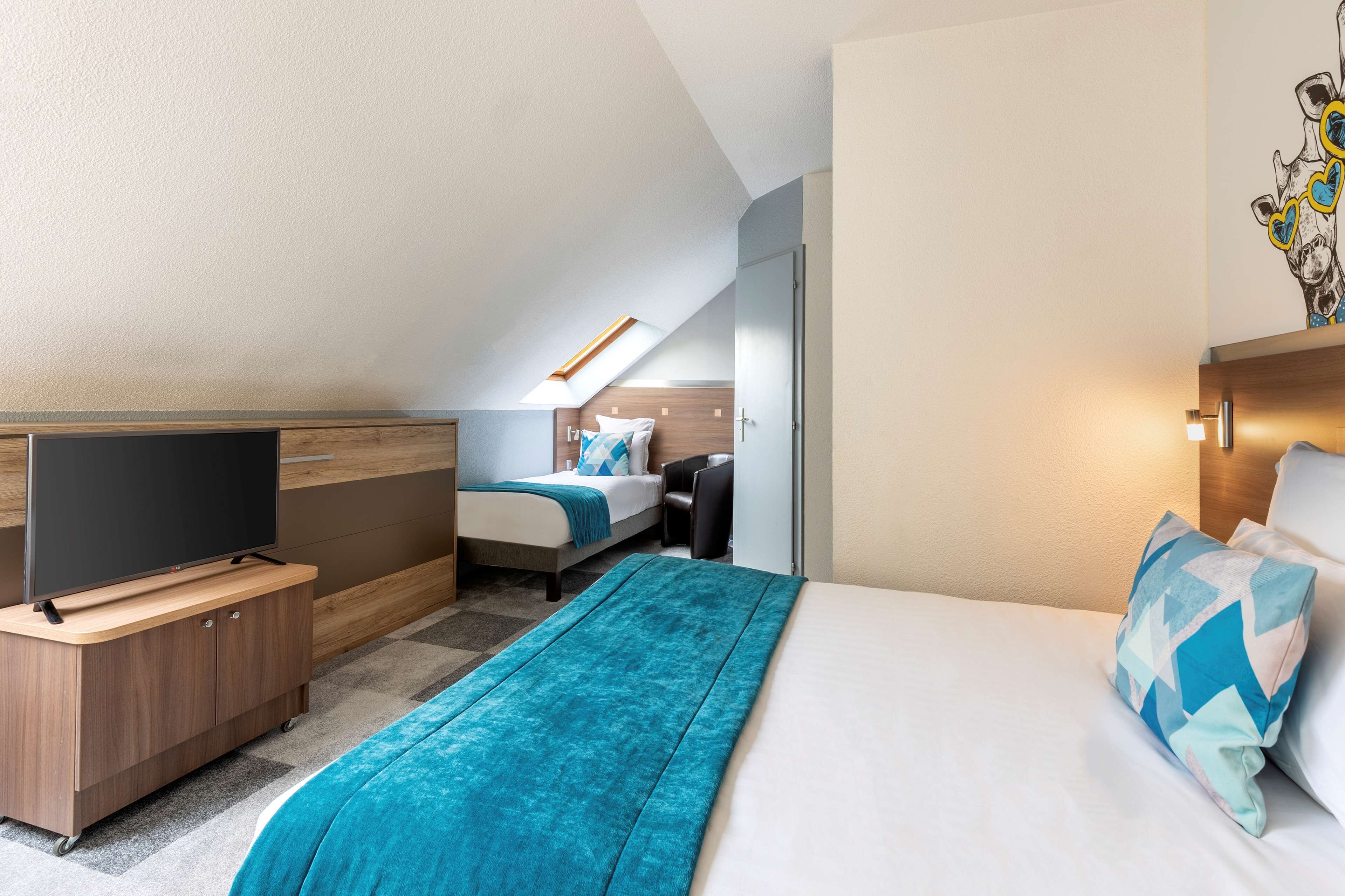 A modern hotel room with a large bed, a television on a wooden stand, a desk, and a small seating area.