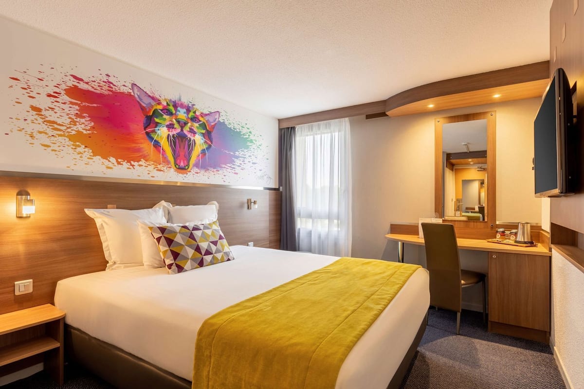 Une chambre d’hôtel comprenant un lit, un bureau, une chaise, un miroir et un tableau au mur.