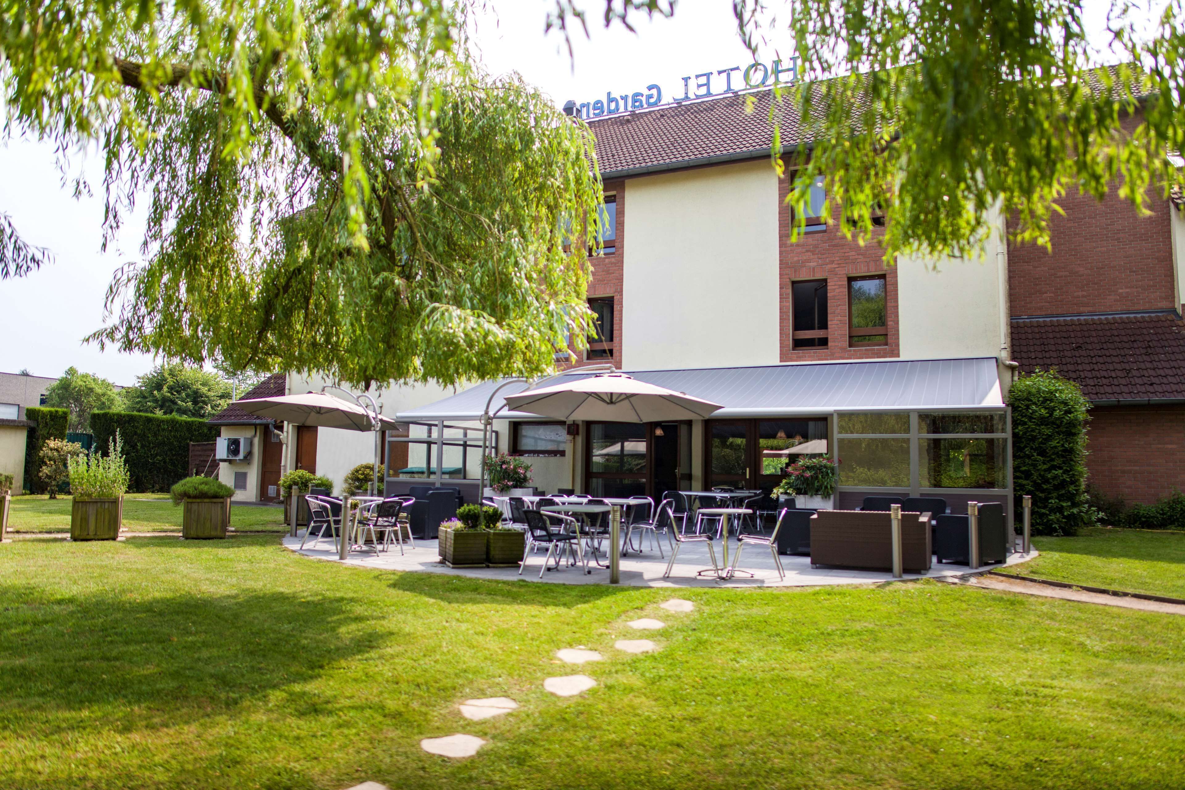 An outdoor seating area with tables and chairs, a covered patio, and a building with a sign that reads "Hotel".