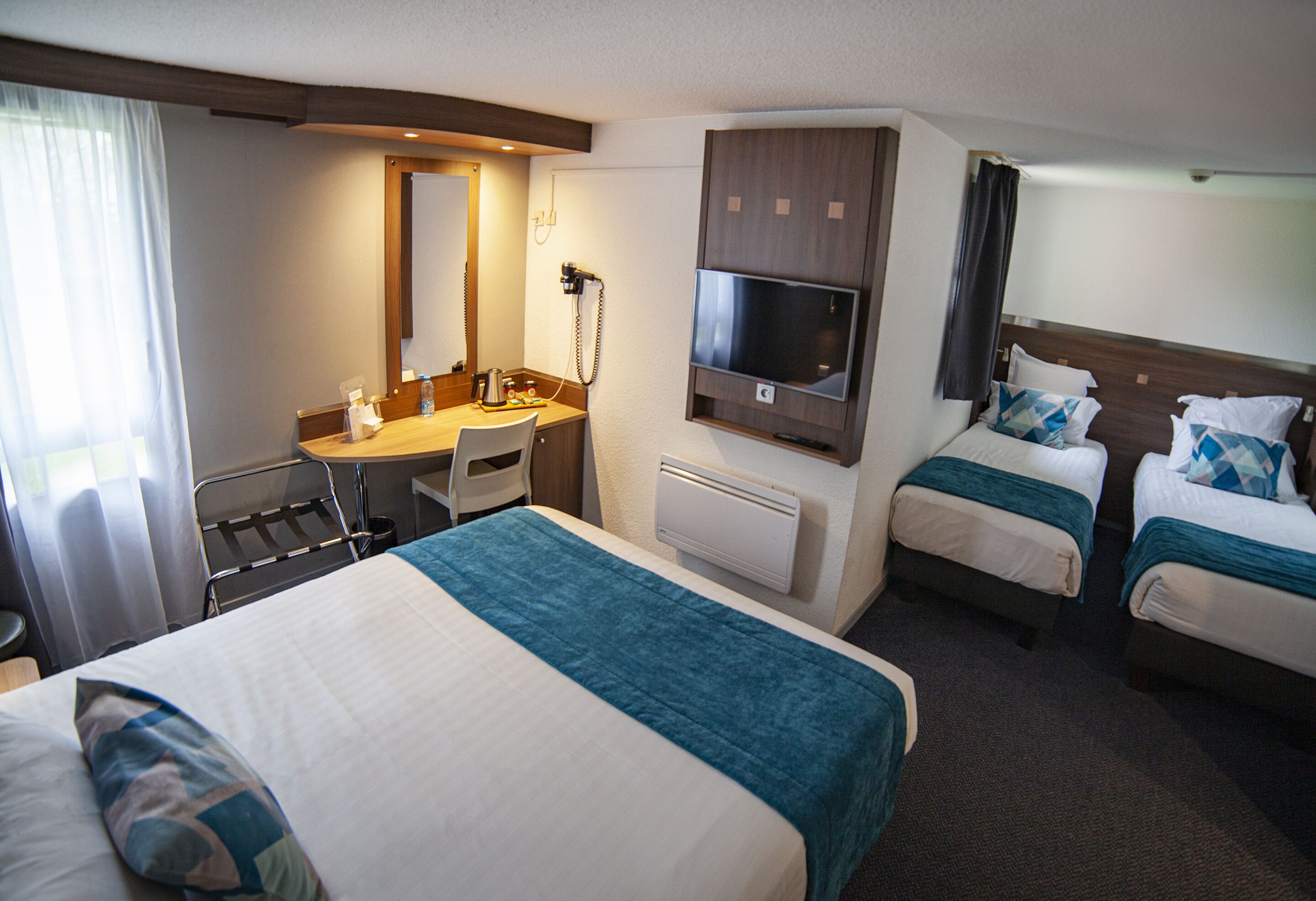 A hotel room with a large bed, a desk with a chair, a TV, and two smaller beds.