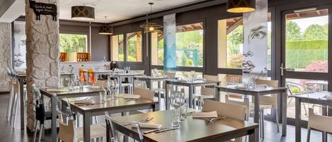 Restaurante com várias mesas, cadeiras e luminárias pendentes.