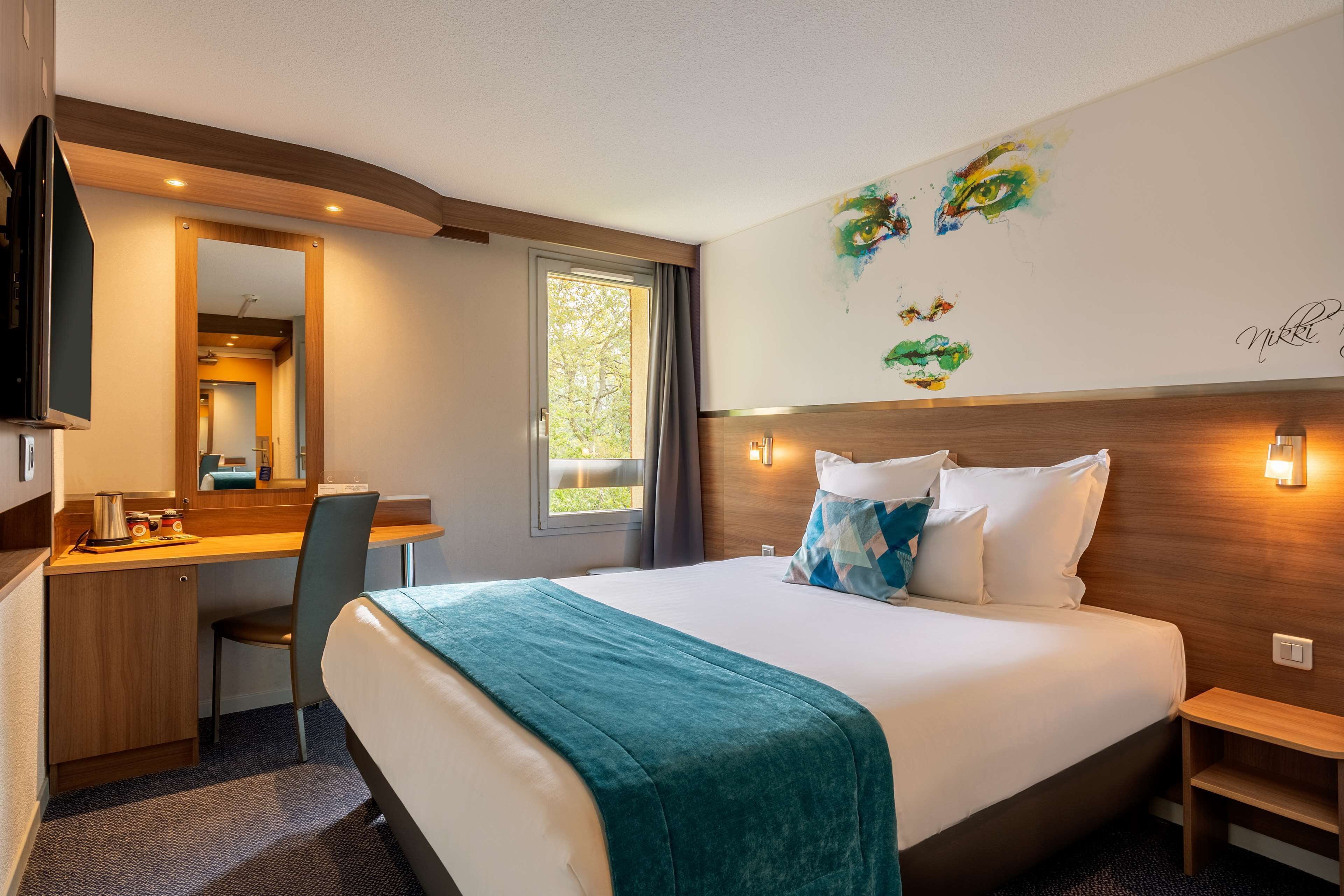 Une chambre d’hôtel avec un lit, un bureau, une chaise et une grande fenêtre.
