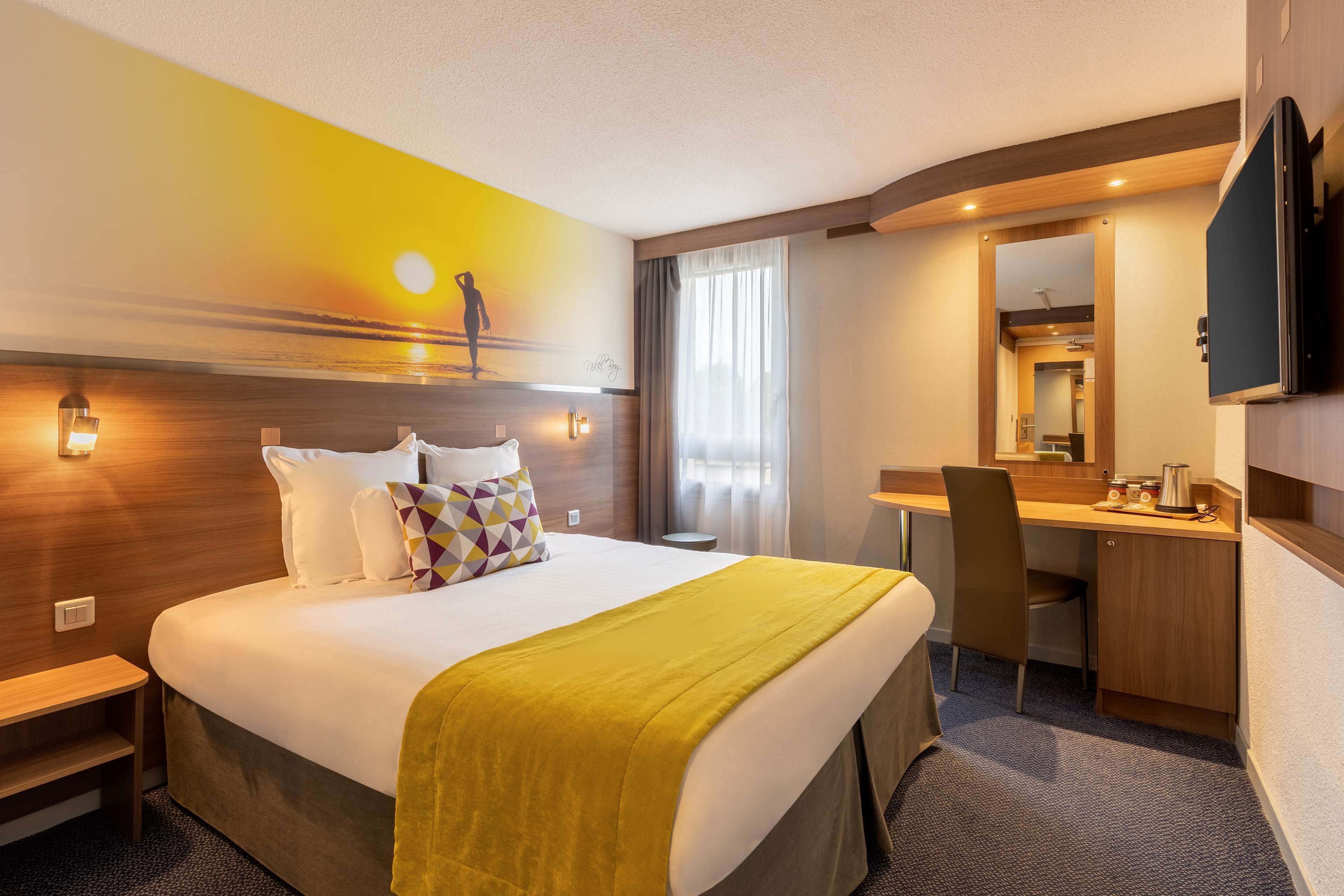Une chambre d’hôtel avec un lit, un bureau, une chaise, une télévision et un tableau au mur.
