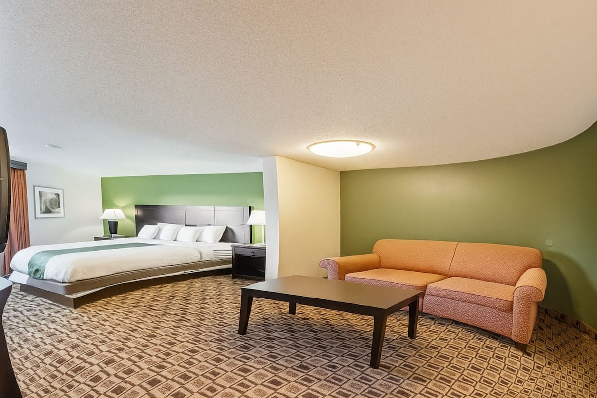 A hotel room with a bed, a sofa, a table, and a patterned carpet.