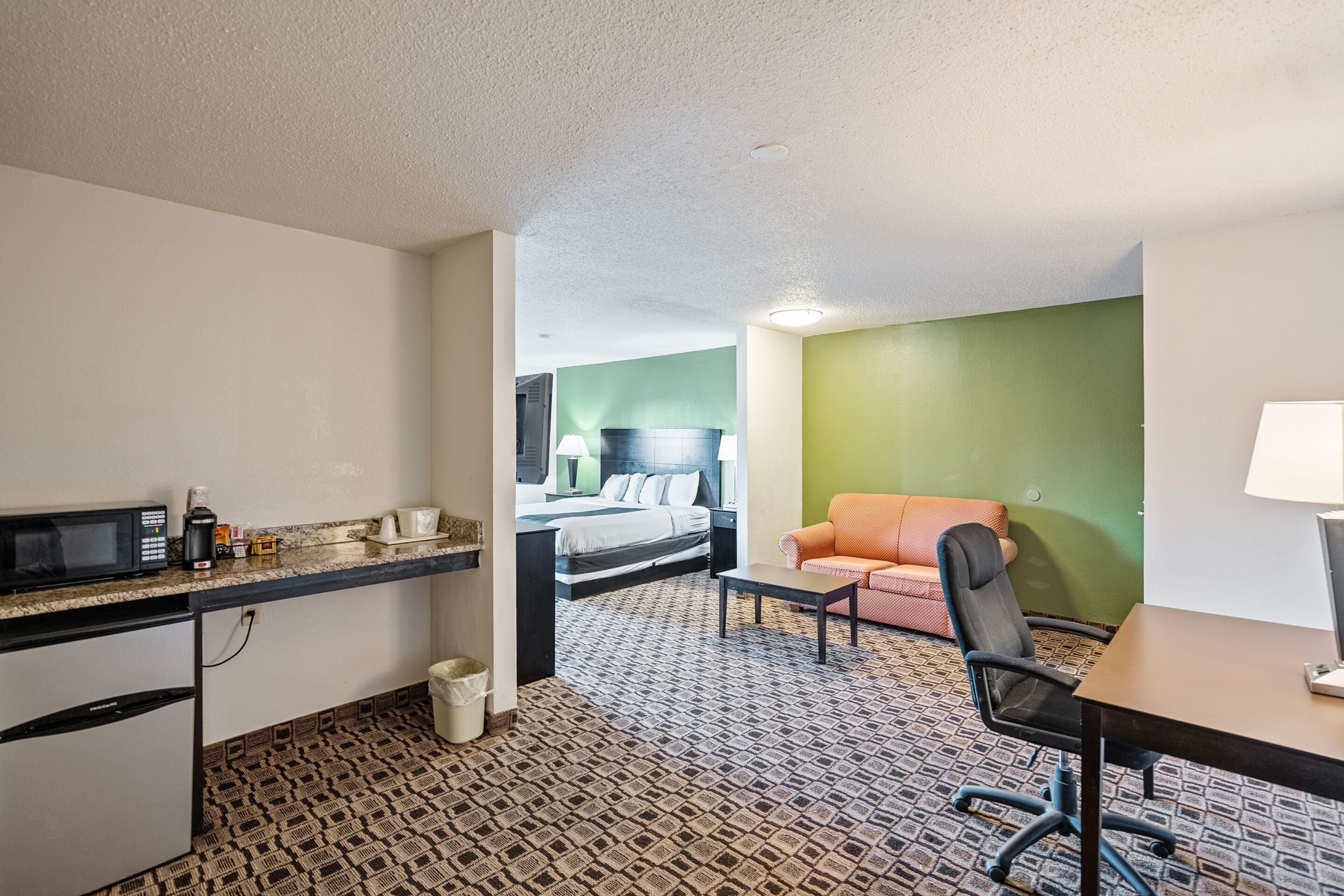 A compact hotel room with a kitchenette, a bed, a desk, and a sofa.
