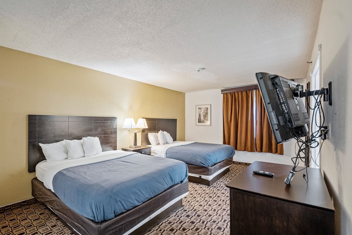 A hotel room with two beds, a desk, a television, and a patterned carpet.