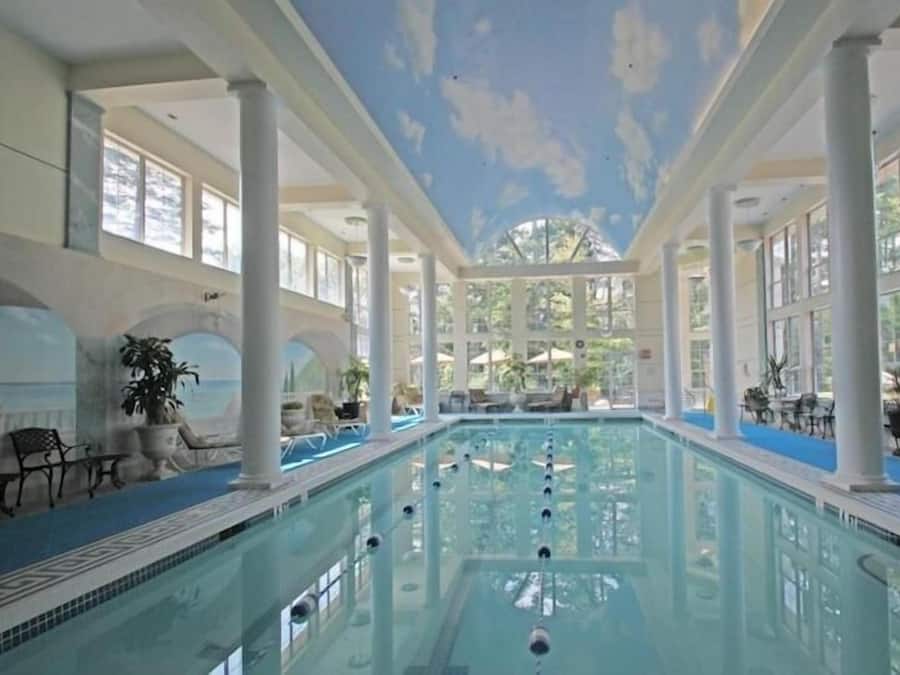 An indoor swimming pool with clear blue water, surrounded by white columns and large windows.