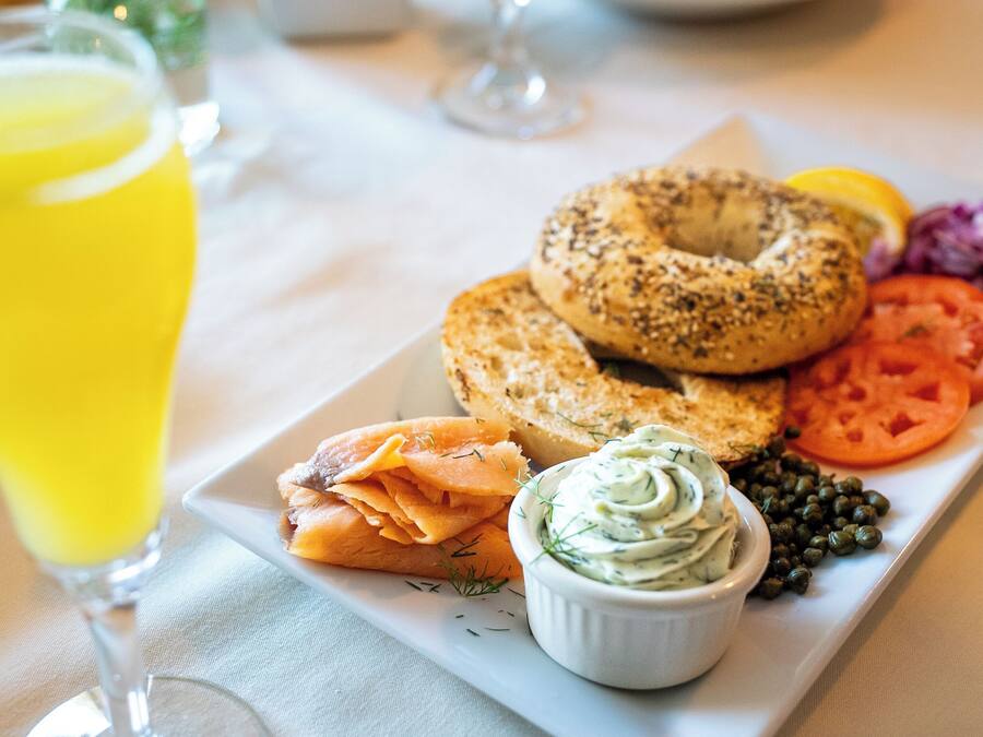 A breakfast plate with bagels, smoked salmon, tomatoes, capers, and a bowl of cream cheese dip.