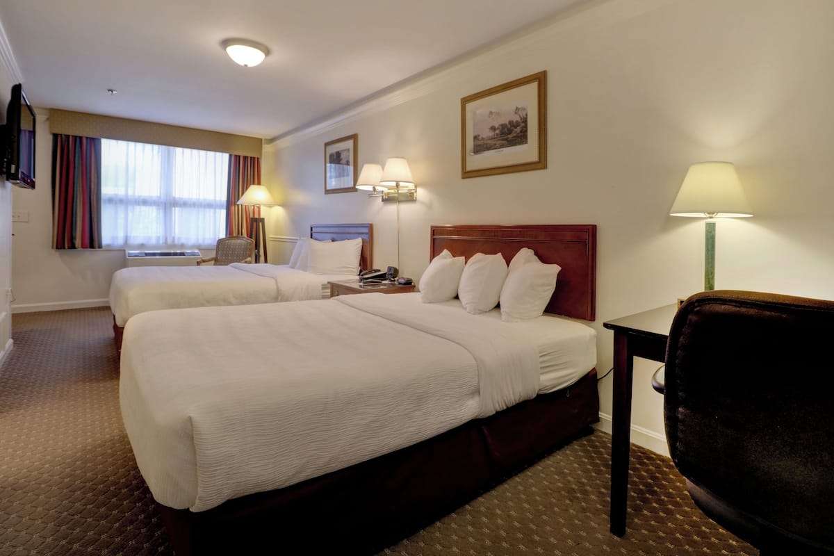 A hotel room with two beds, a desk, a chair, a TV, and a window with curtains.