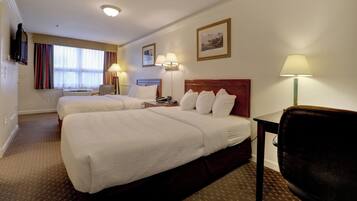 A hotel room with two beds, a desk, a chair, a TV, and a window with curtains.