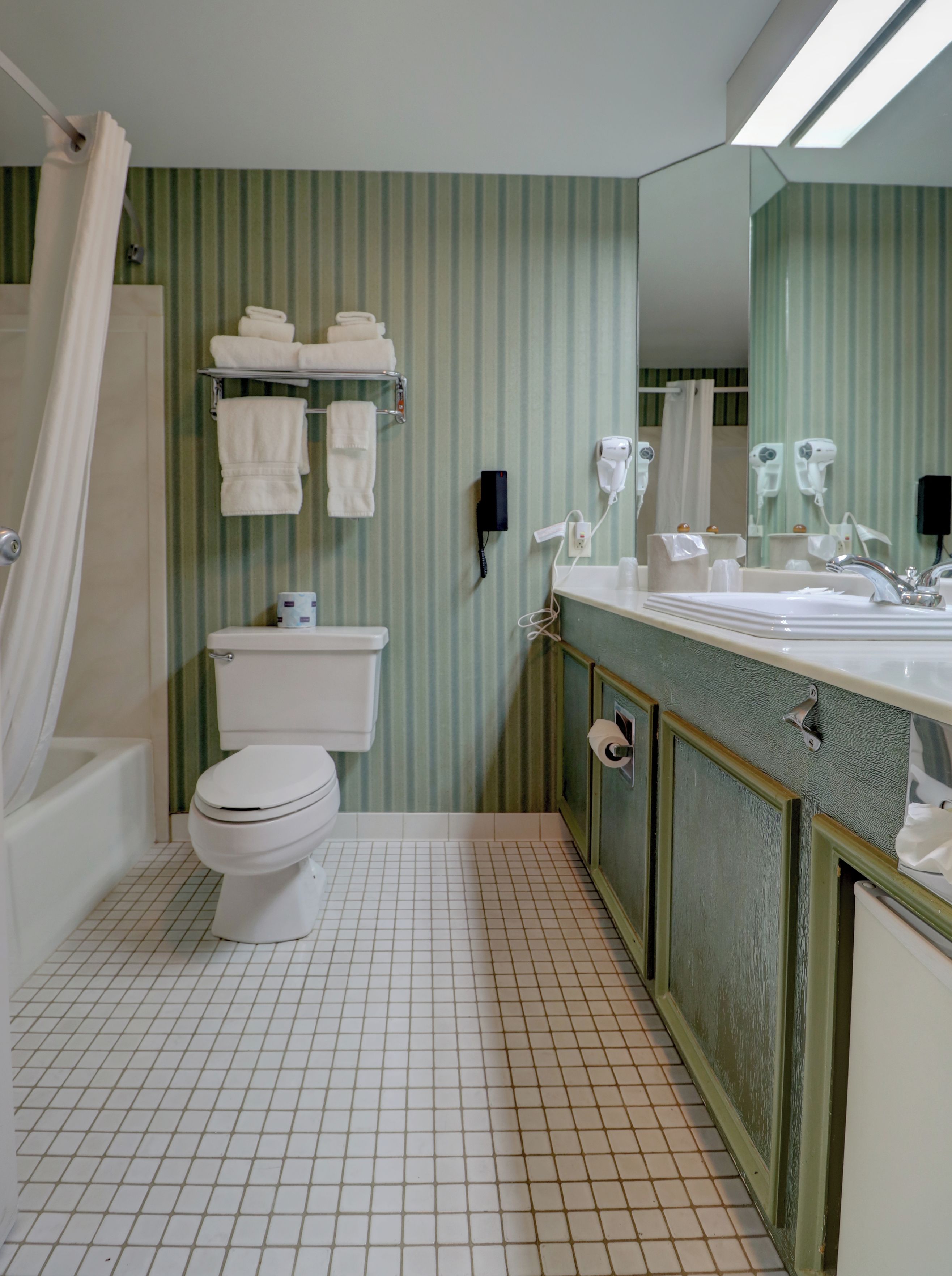 A bathroom with a toilet, a bathtub, a shower curtain, a towel rack with towels, a mirror, and a sink with a faucet.