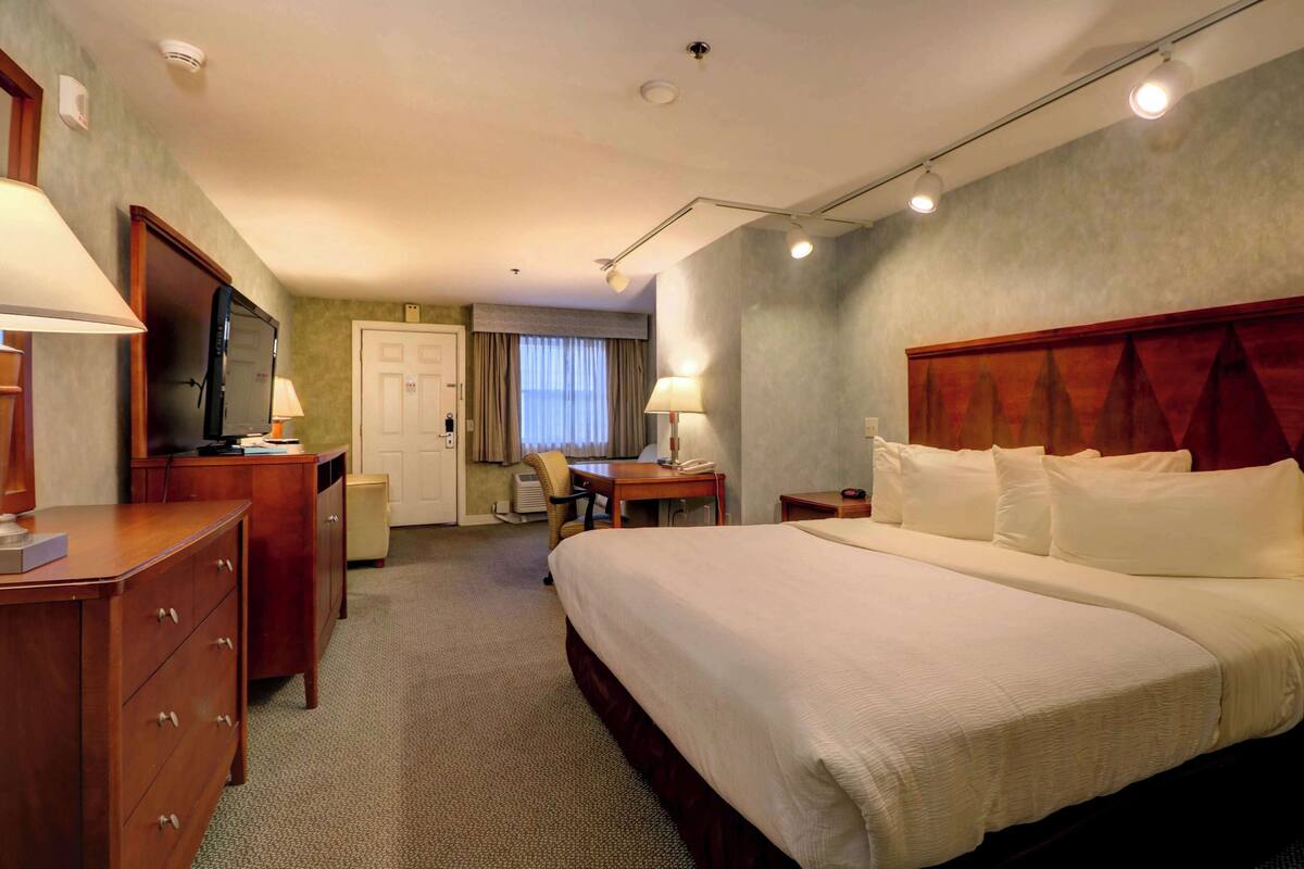 A hotel room with a large bed, a desk, a chair, a television, and a wardrobe.