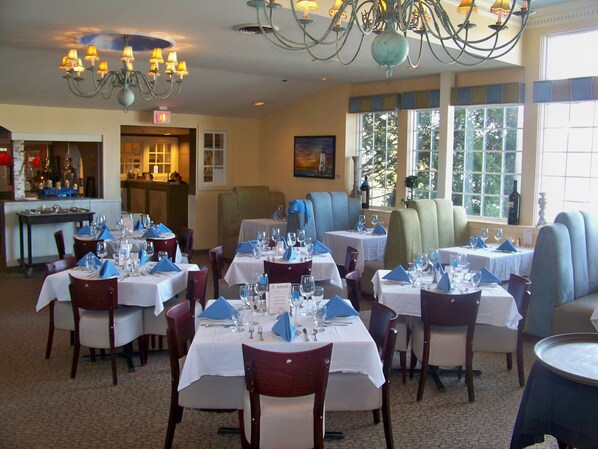 A restaurant with multiple tables set for dining, a bar area, and large windows with a view of trees.