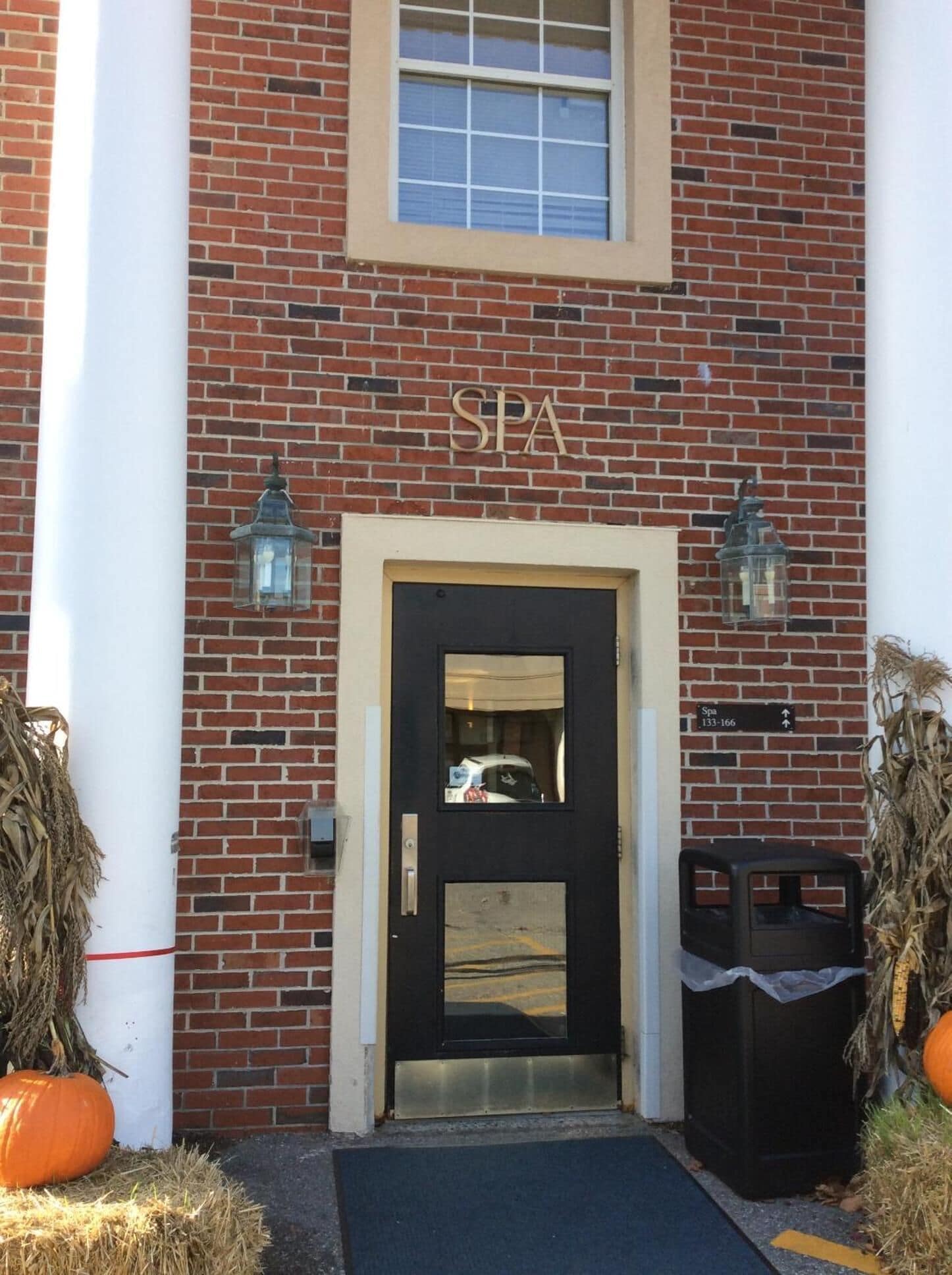 A brick building with a black door, labeled "SPA," and two lantern-style lights.