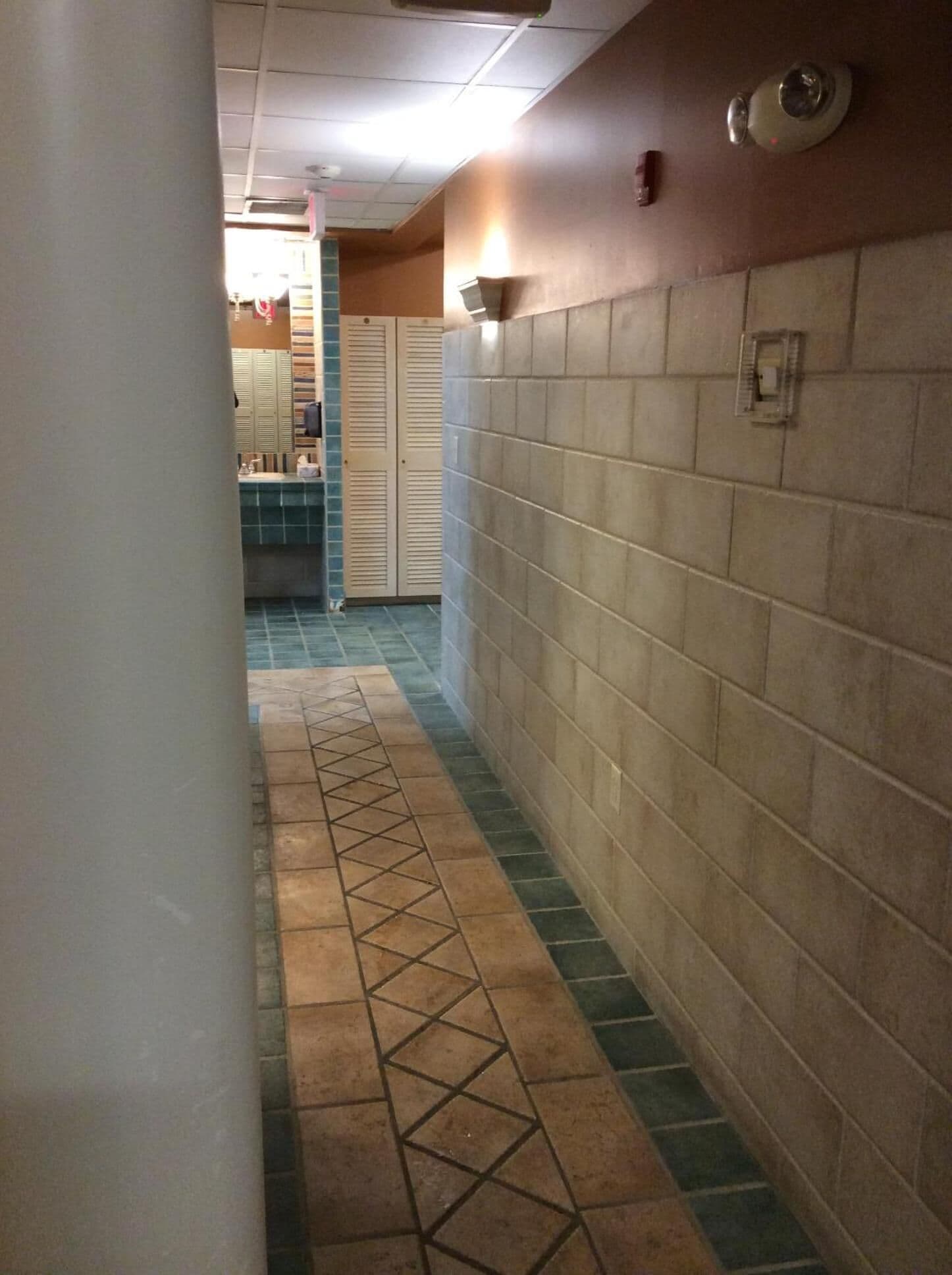 A corridor with tiled walls and floor, leading to a room with a tiled backsplash and a sink.
