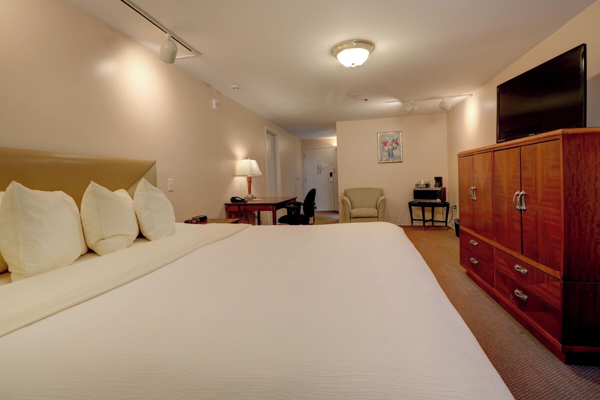 Une chambre d’hôtel avec un grand lit, une armoire en bois, un bureau avec une chaise, une télévision et un tableau au mur.