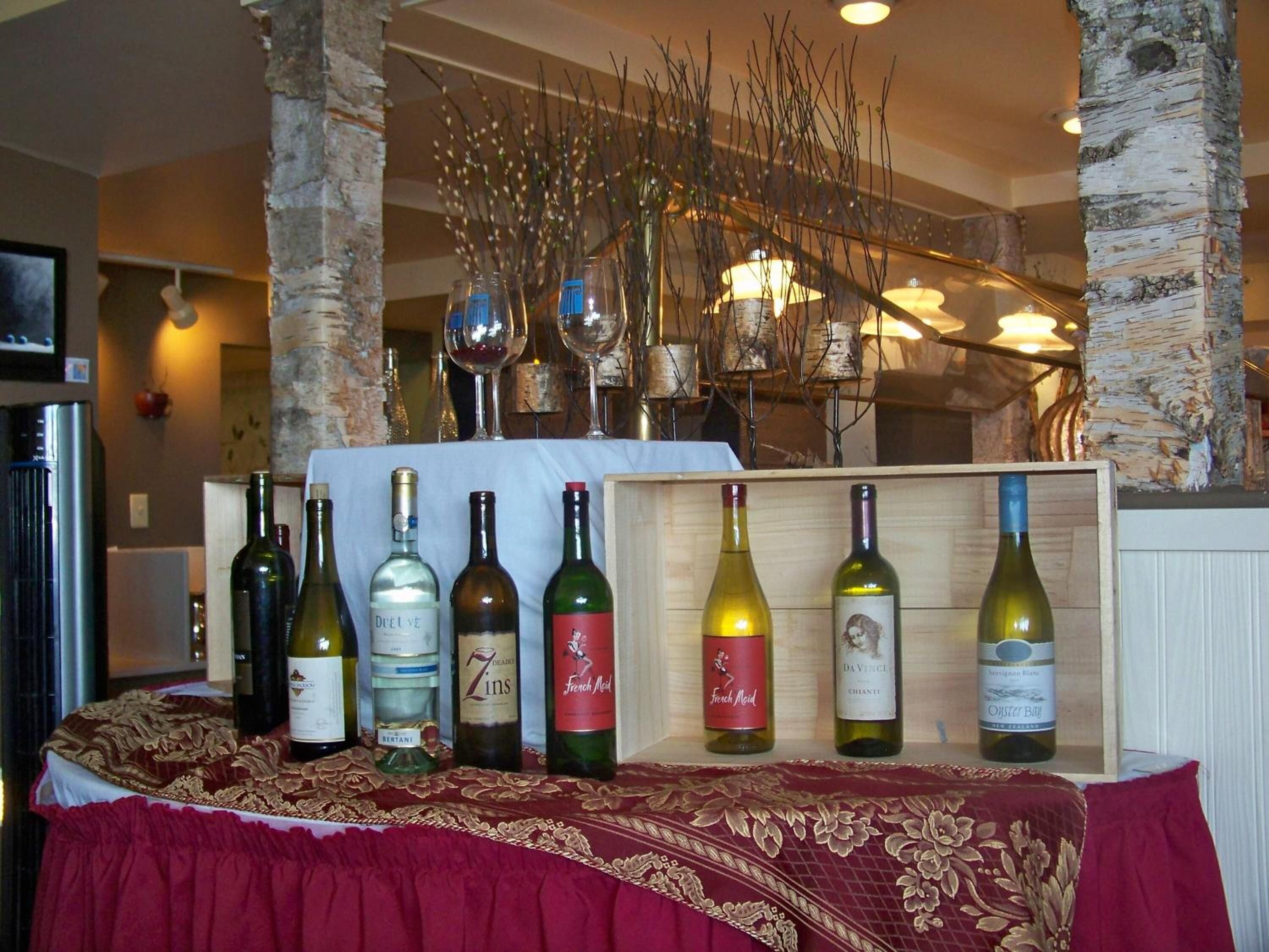 A wine display with bottles on a table, surrounded by birch tree trunks and decorative branches.
