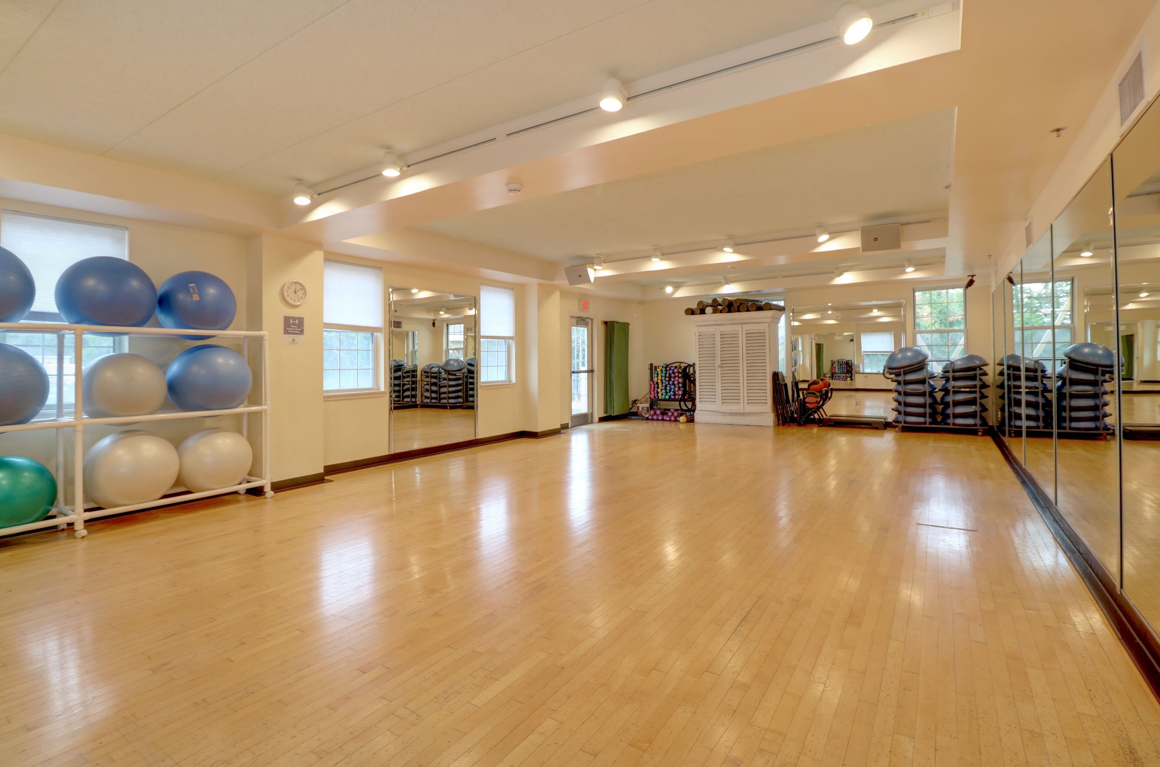 A spacious room with wooden flooring, exercise balls, and mirrors.