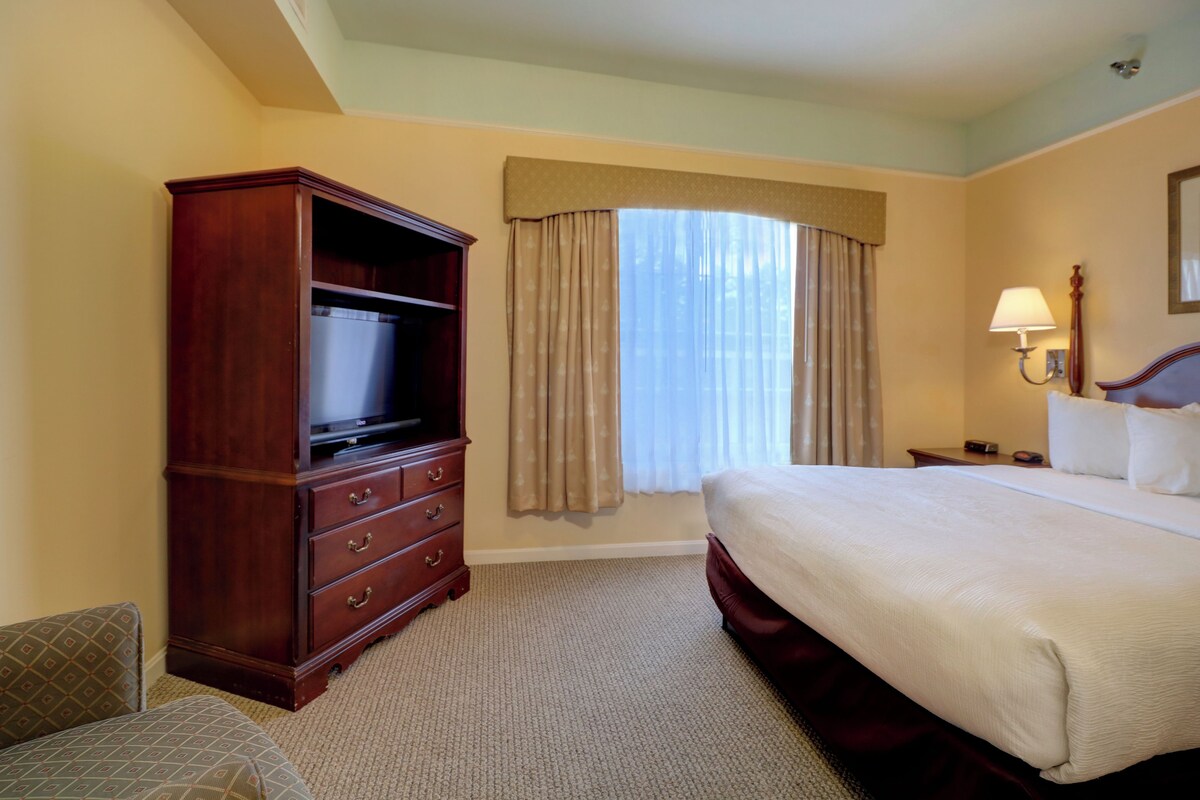 Une chambre d’hôtel avec un grand lit, une commode en bois, une télévision et une fenêtre avec des rideaux.