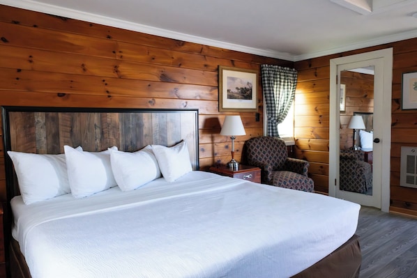 A wooden-paneled room with a large bed, a chair, a nightstand, and a door with a mirror.