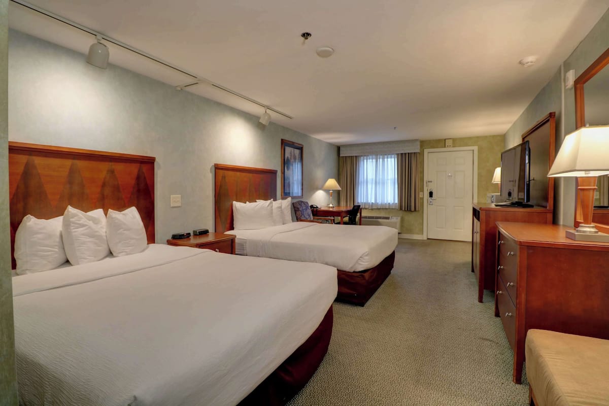 A hotel room with two beds, a desk, a chair, a dresser, and a mirror.