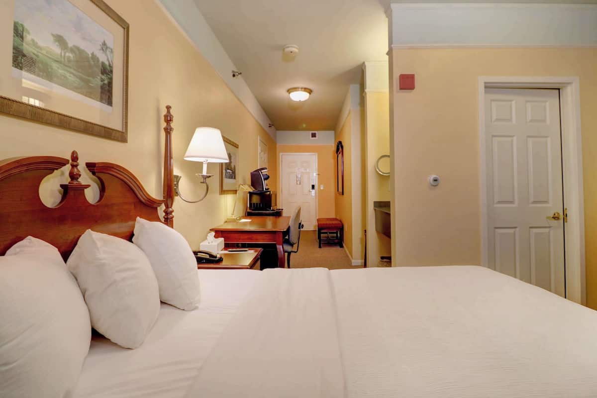 A hotel room with a large bed, a desk with a lamp, a chair, a television, and a door.
