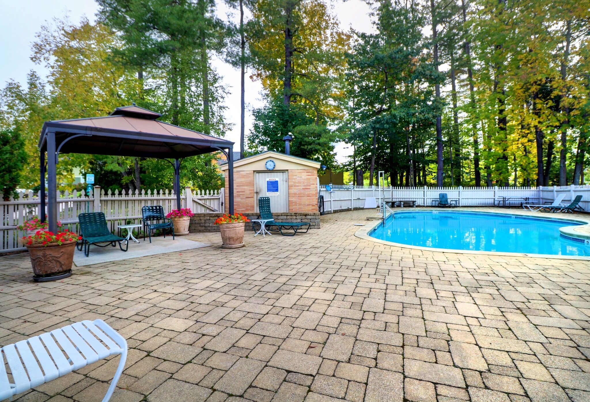 A poolside area with a covered seating area, a small building, and a fenced pool.