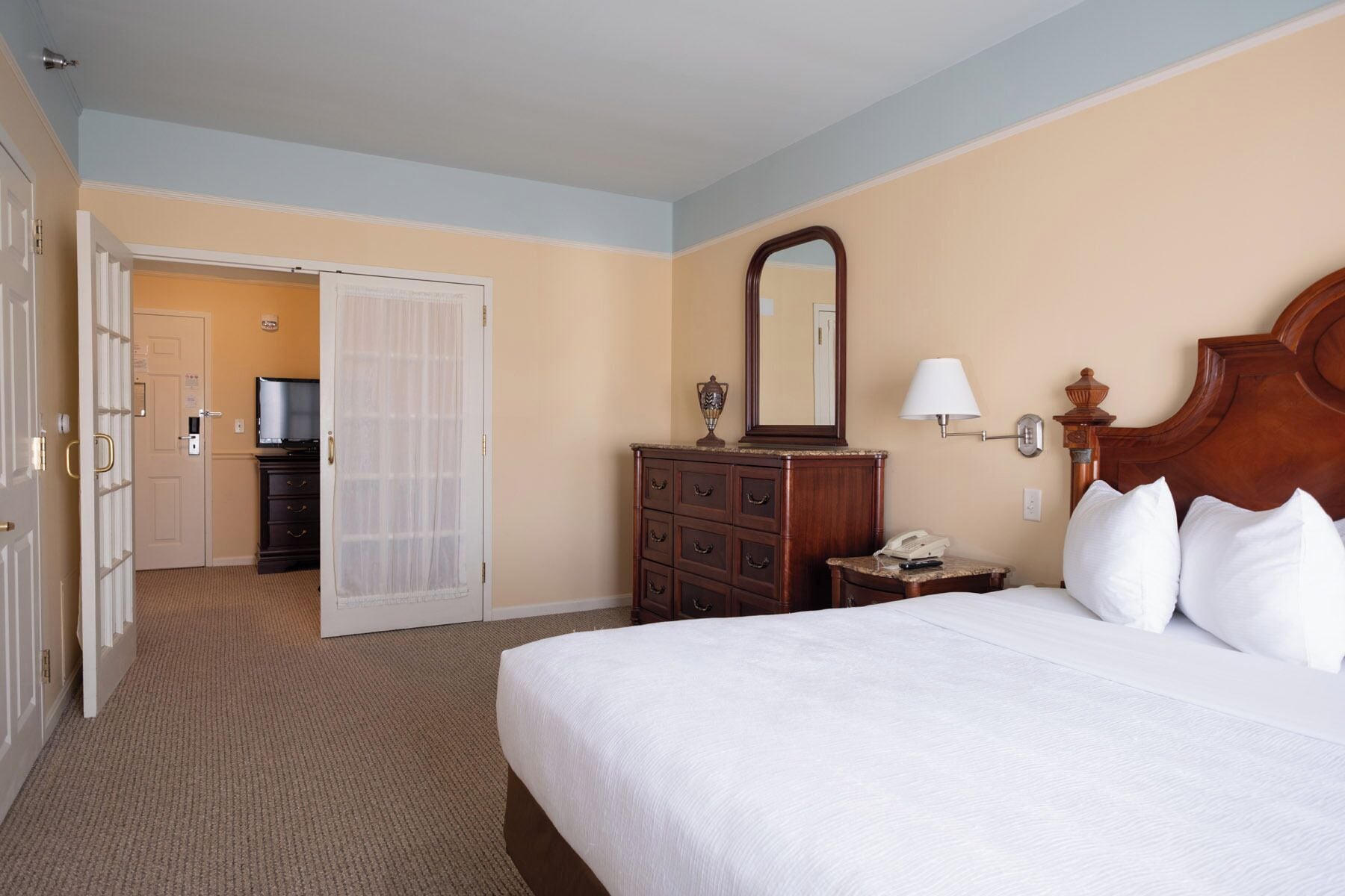 A hotel room with a bed, a dresser, a mirror, a nightstand, a lamp, and a television in the corner.