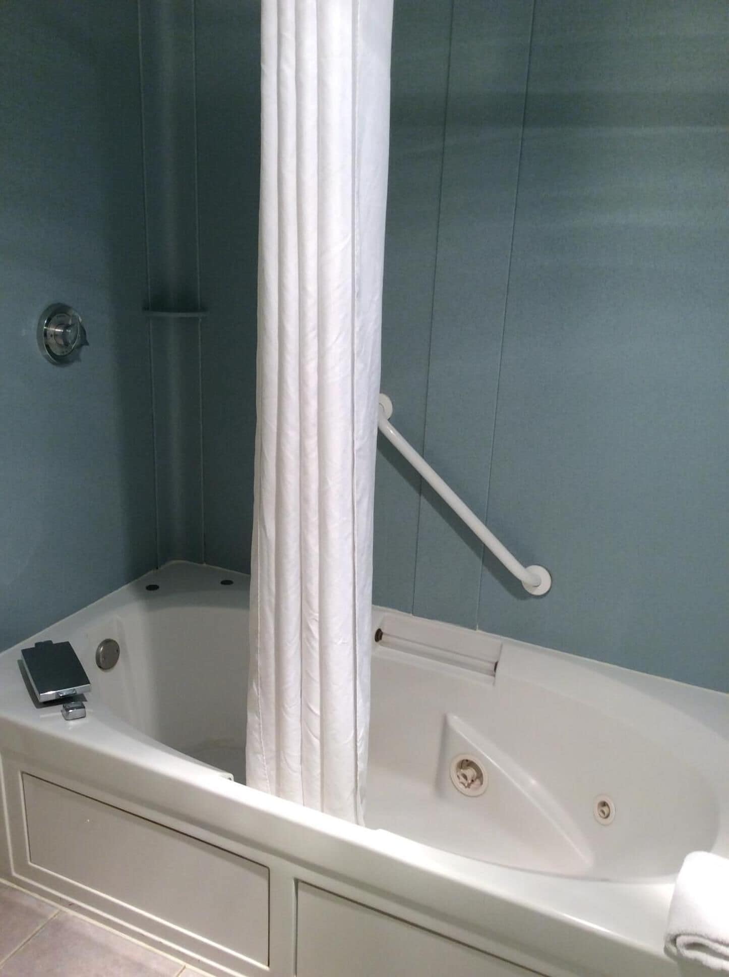A bathroom with a bathtub, a shower curtain, a grab bar, and a towel rack.