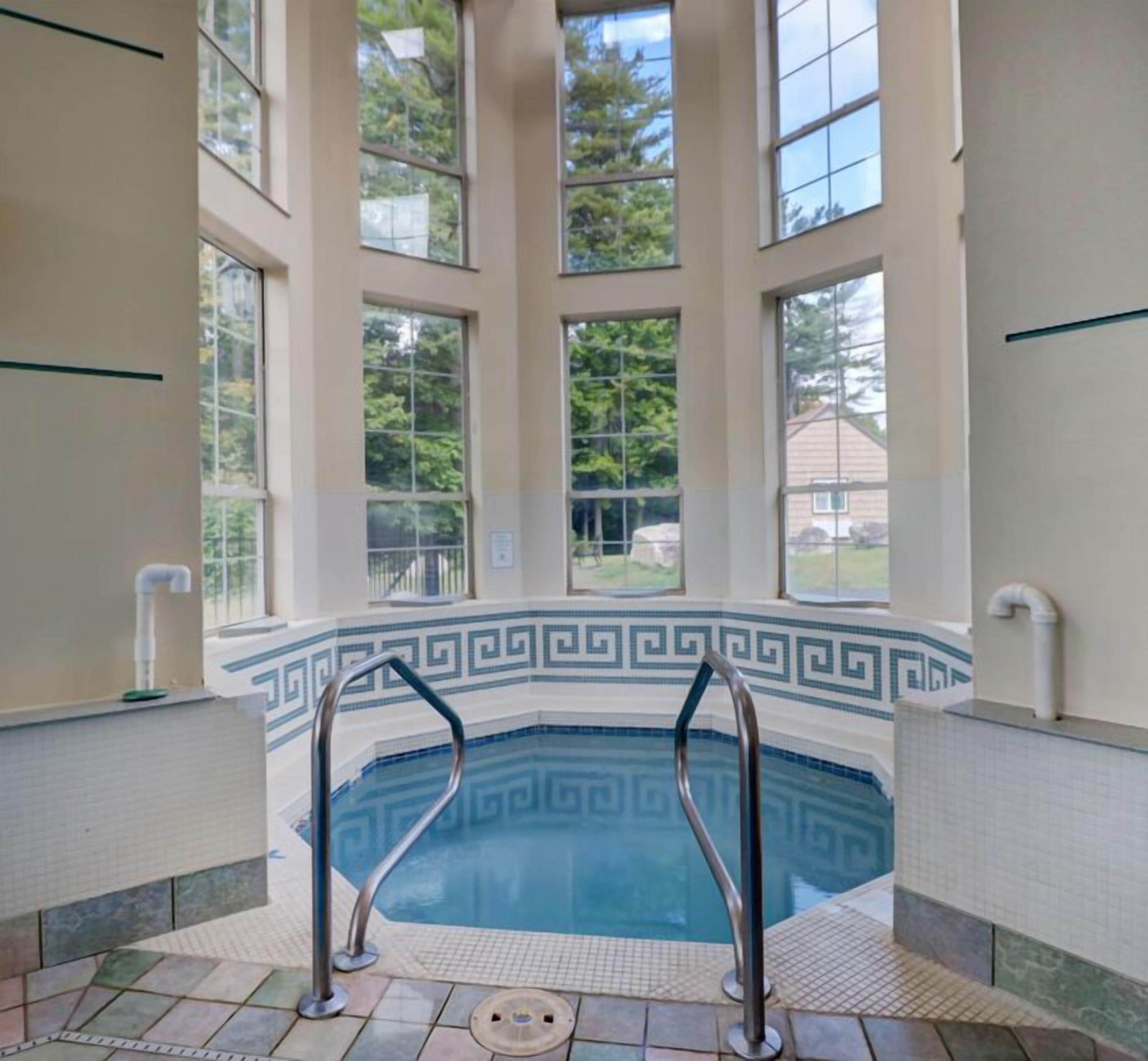 An indoor swimming pool with a geometric tile border, large windows, and a view of the outdoors.
