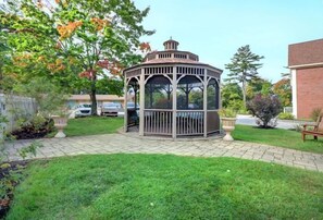A gazebo with a hexagonal shape and a cupola, surrounded by a well-maintained lawn and potted plants.