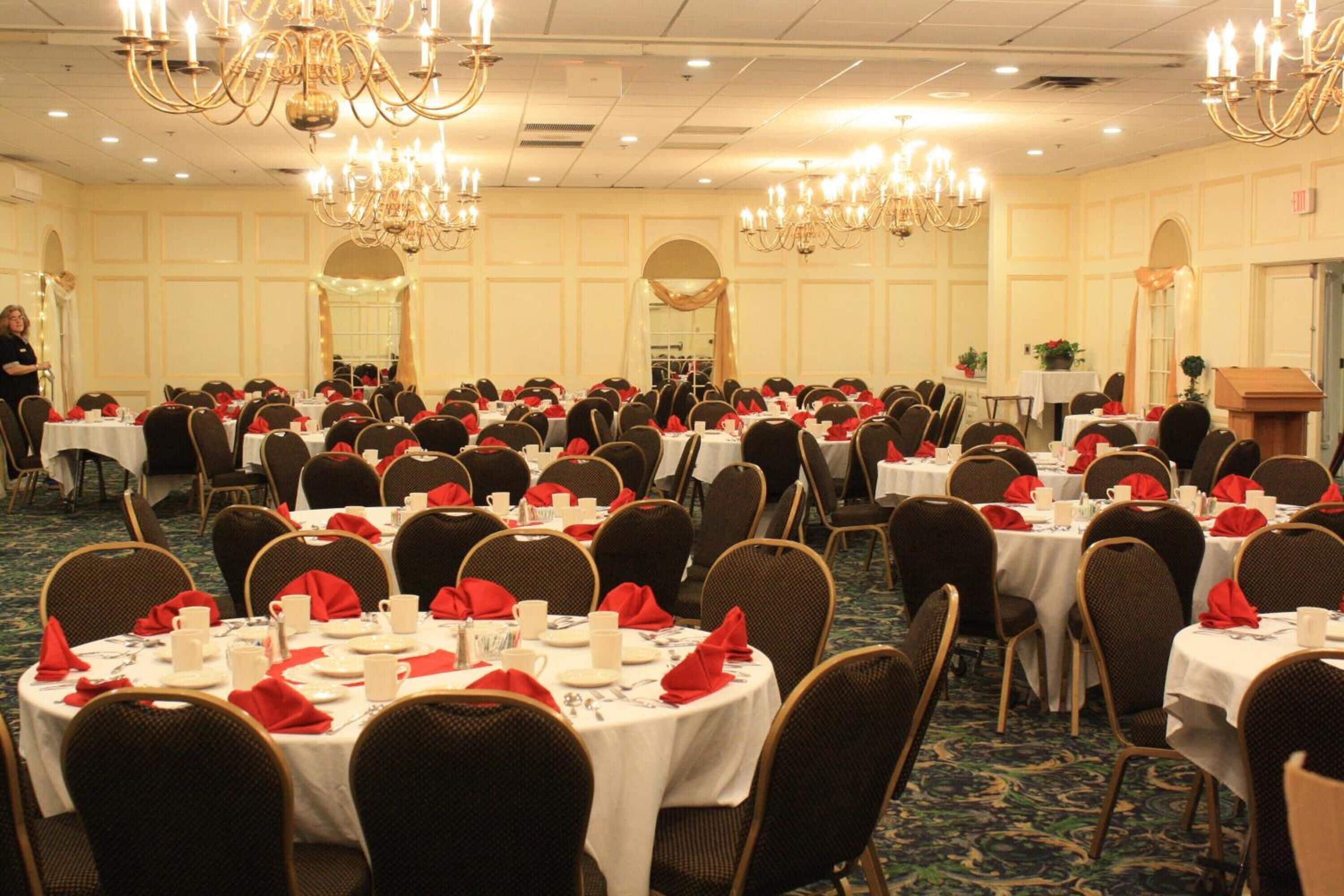 Un salón de banquetes con mesas redondas dispuestas para un evento formal, con candelabros y suelo alfombrado.